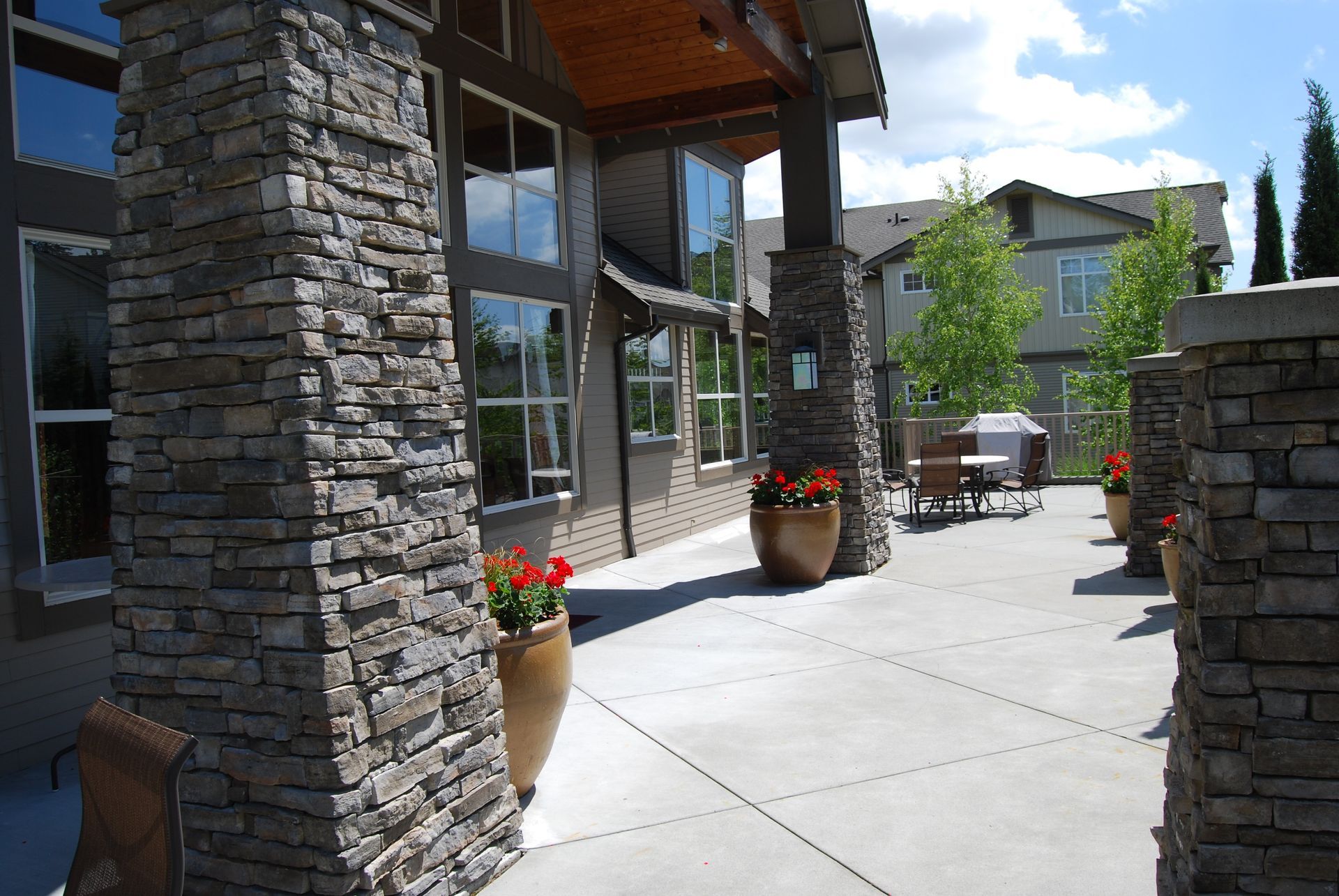 Stone patio with large planters beside a building with glass windows and outdoor tables