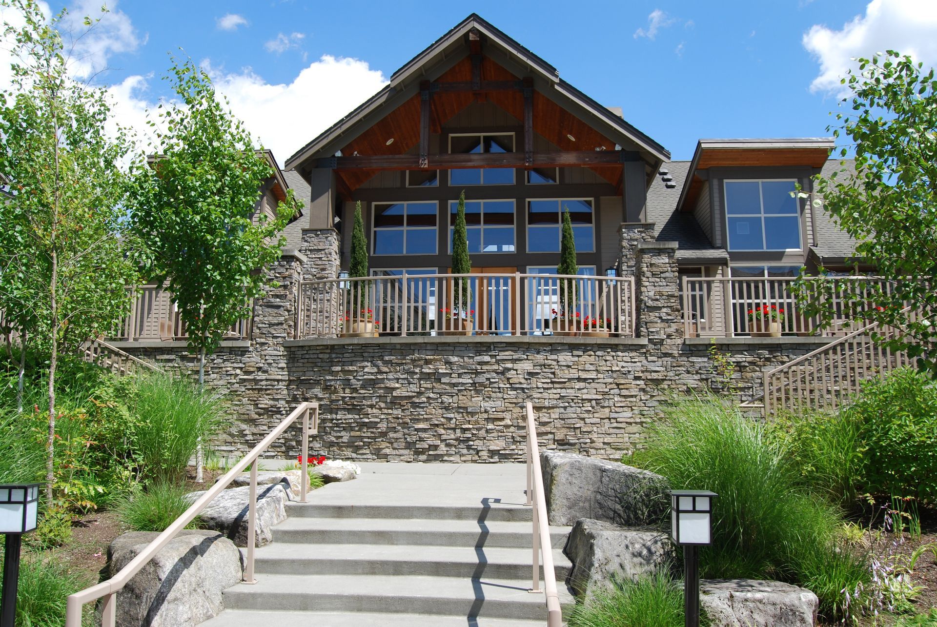 Stone steps lead to a rustic mountain lodge with wooden balconies under a bright blue sky.