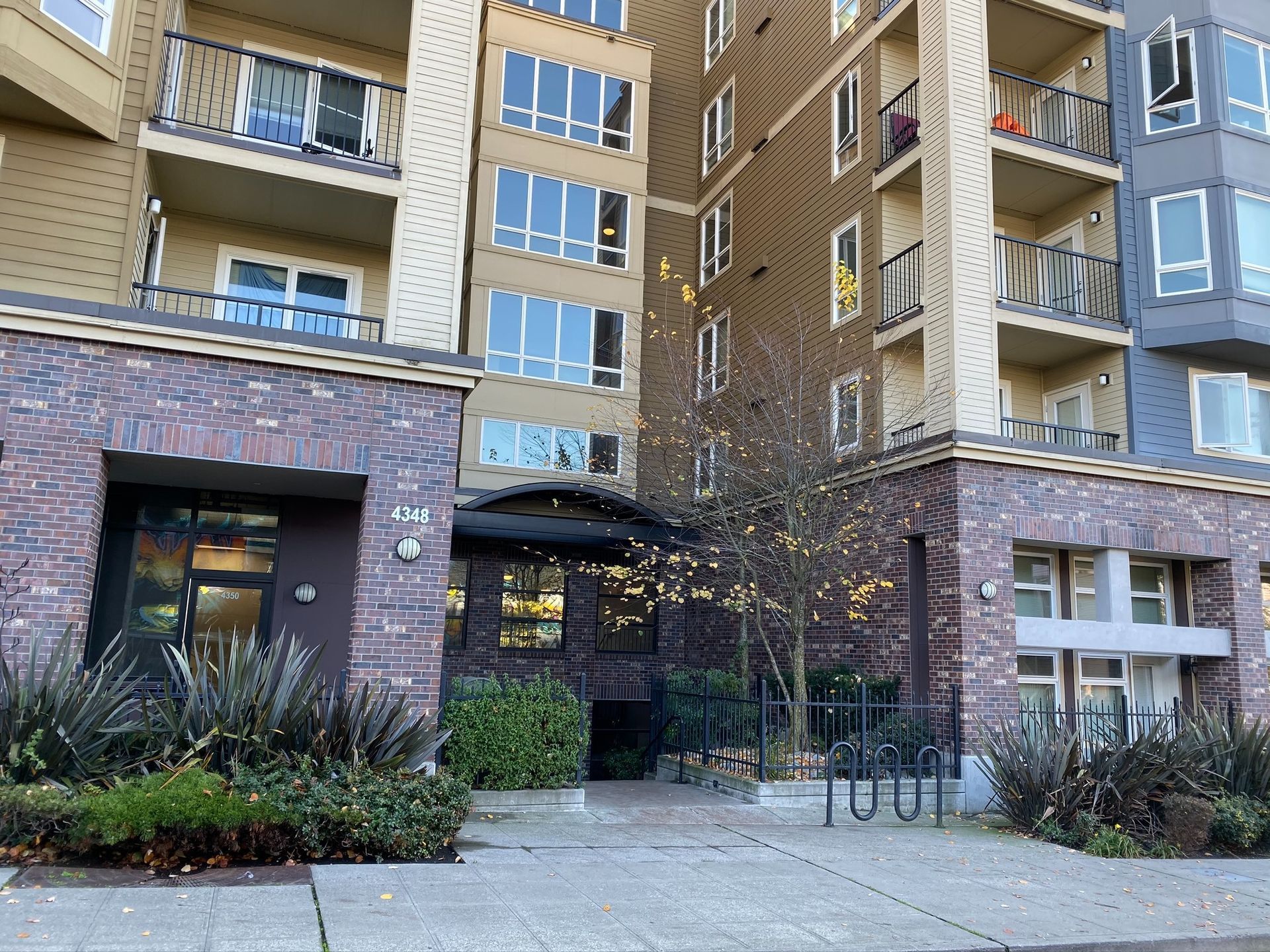 Apartment building entrance with brick facade, balconies, and landscaped walkway.