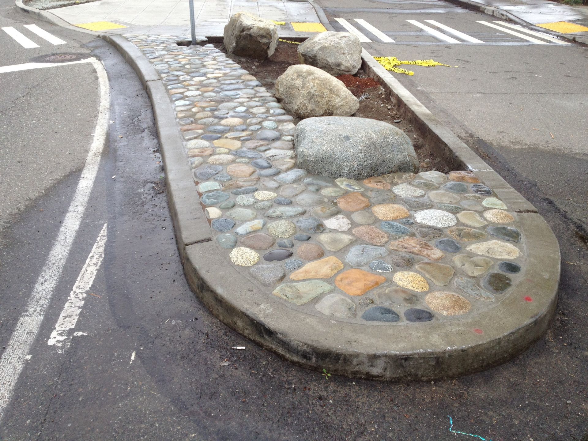 Stone-lined traffic island with colorful circular paving and large rocks beside a crosswalk