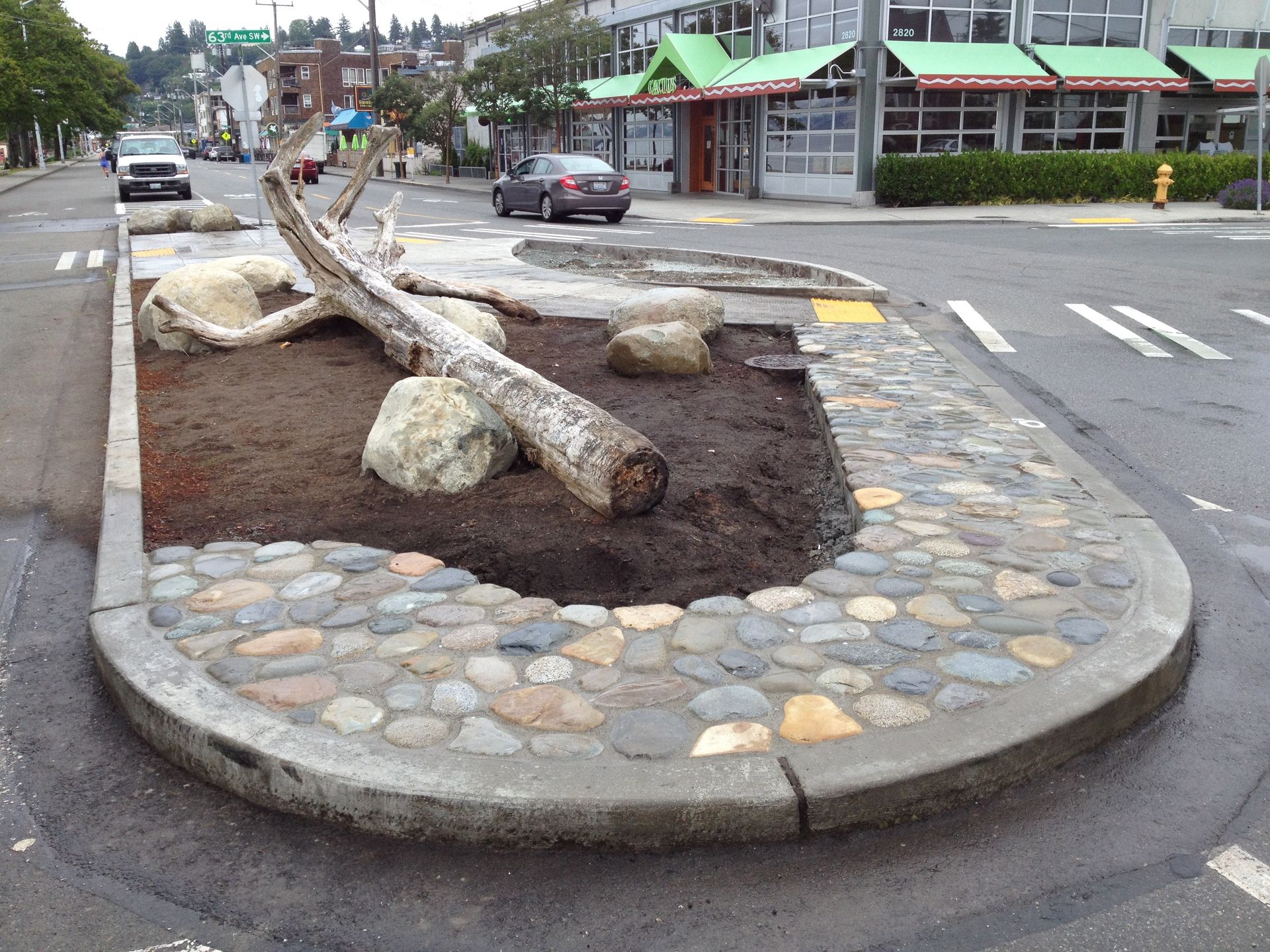 Roadside landscaped traffic island with logs, rocks, and stone border at an intersection