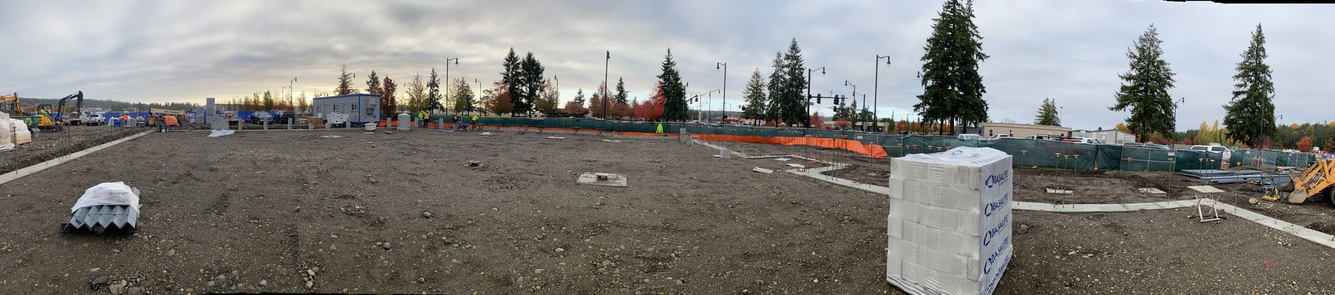 Wide gravel lot with scattered cars, a concrete barrier, and trees under an overcast sky.