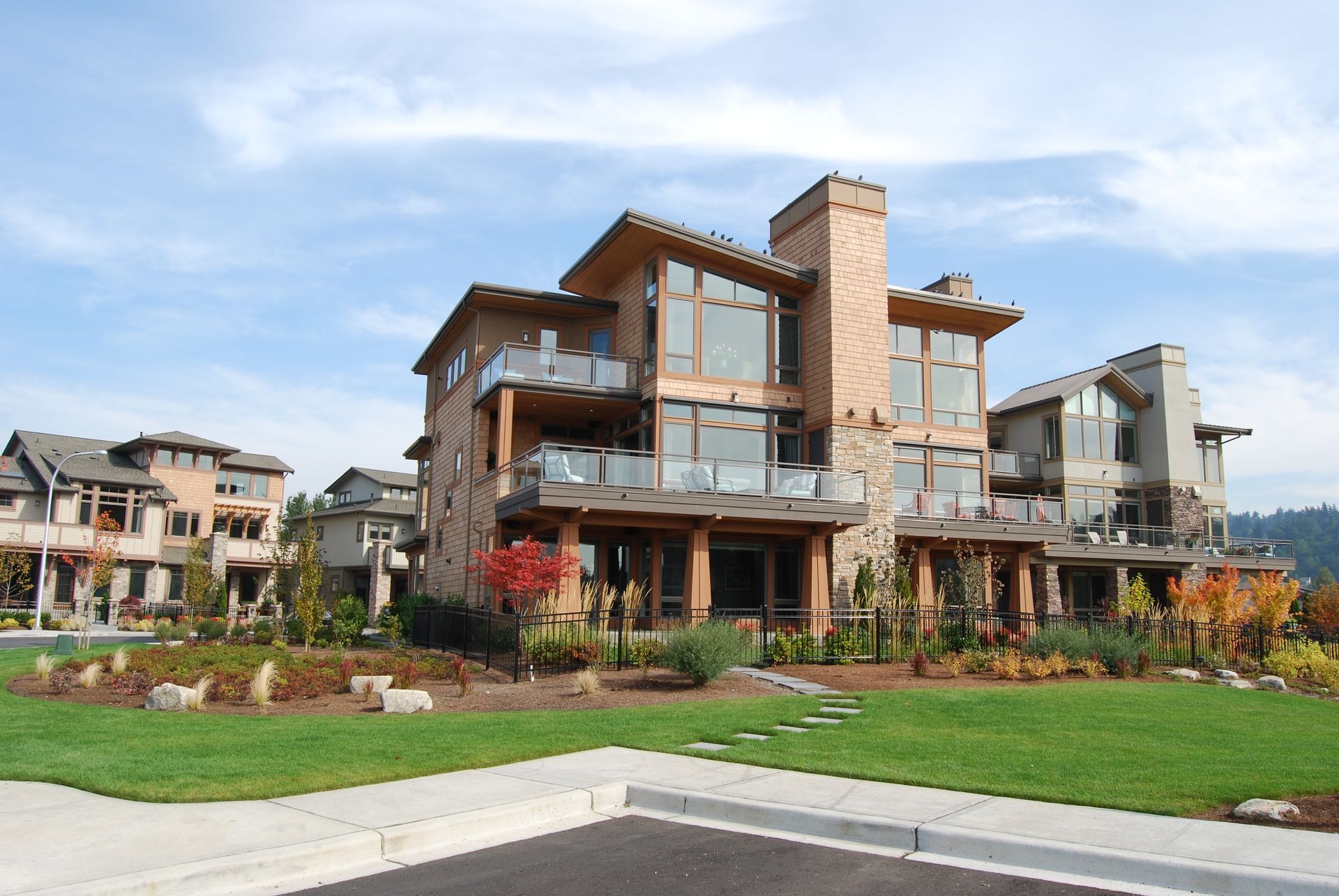 Modern multi-story apartment building with wood accents, large windows, and landscaped lawn under a blue sky