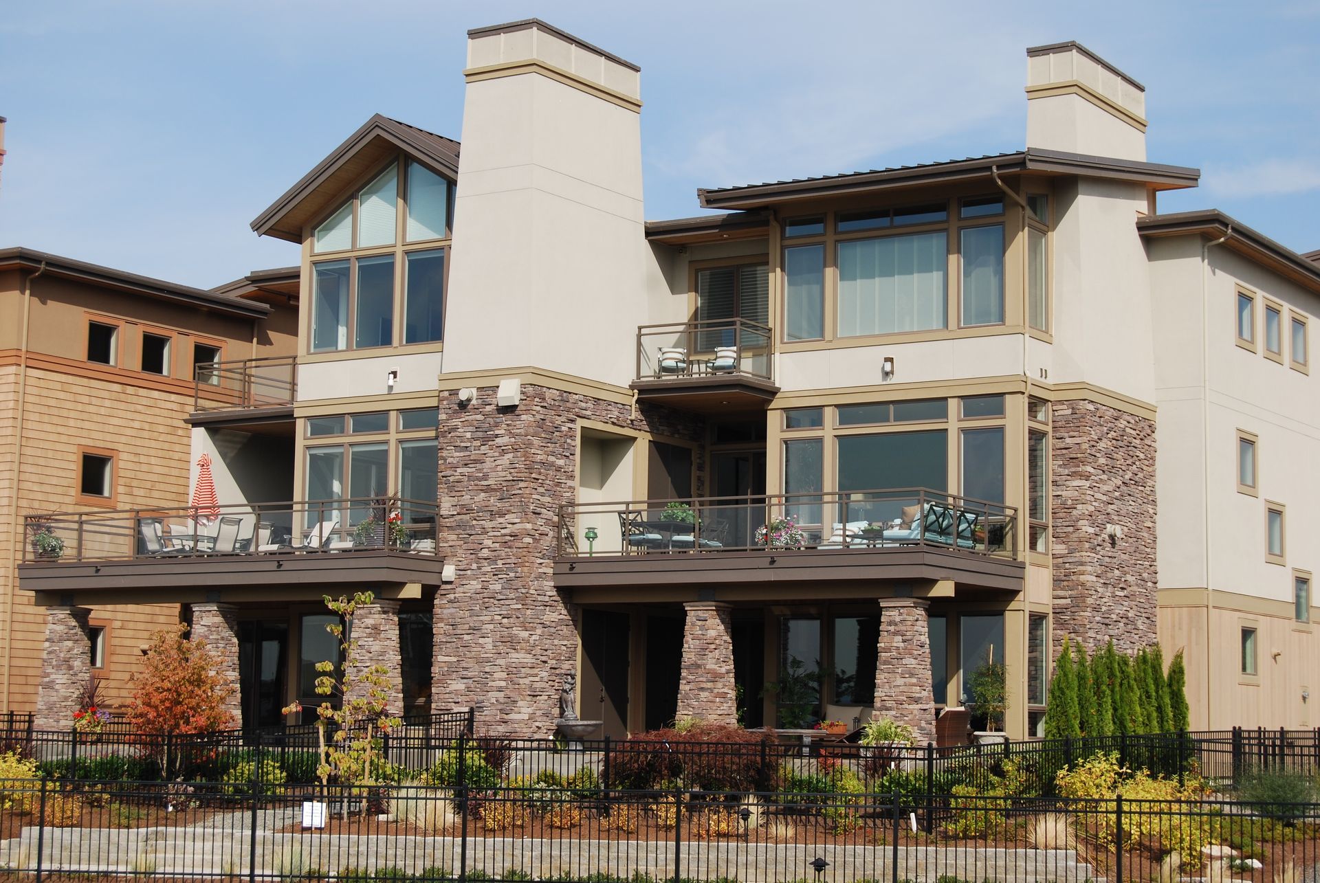 Modern two-story townhouse with balconies, stone accents, and tall chimneys behind a black fence