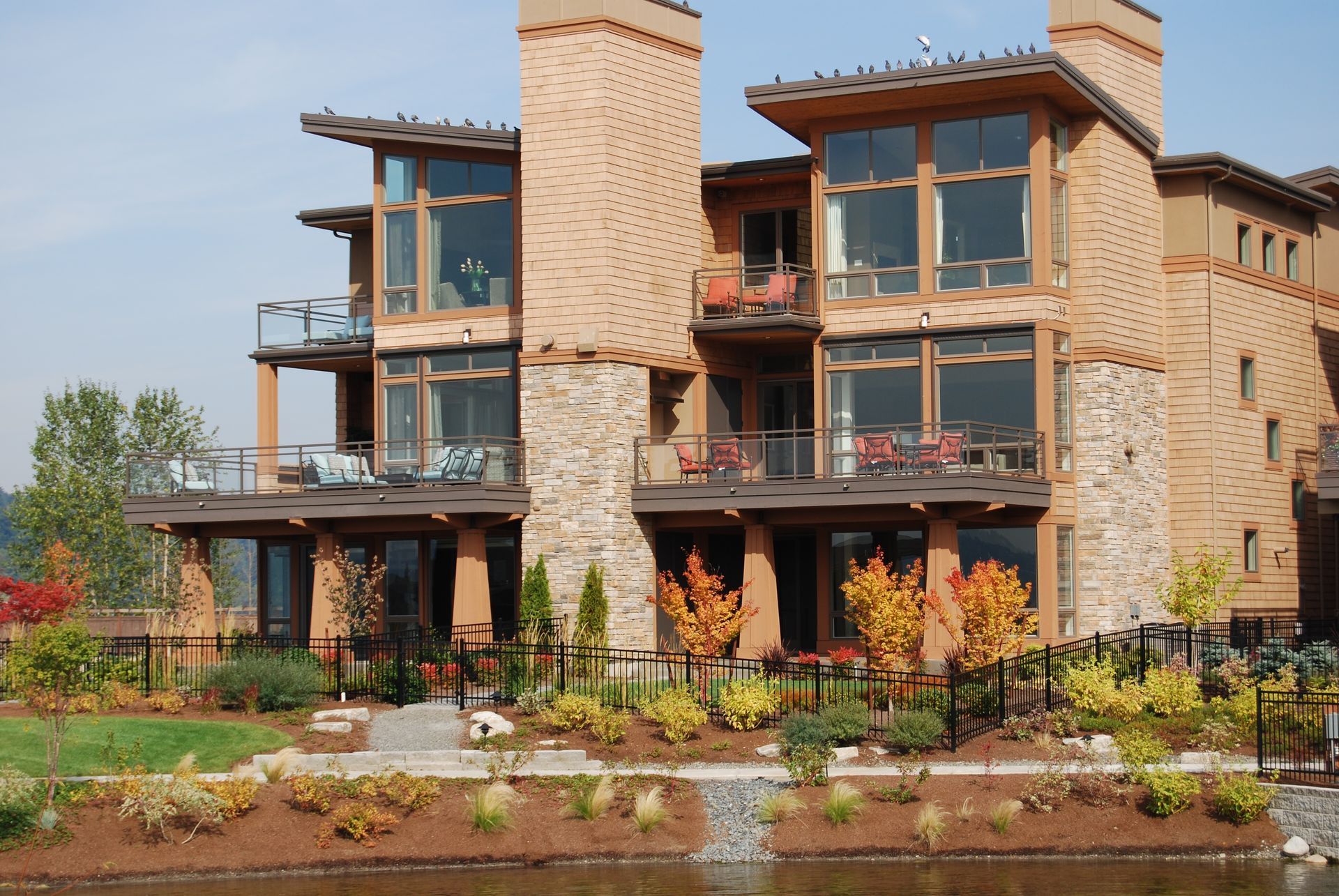 Modern stone lodge with balconies and chimney beside a landscaped pond and garden