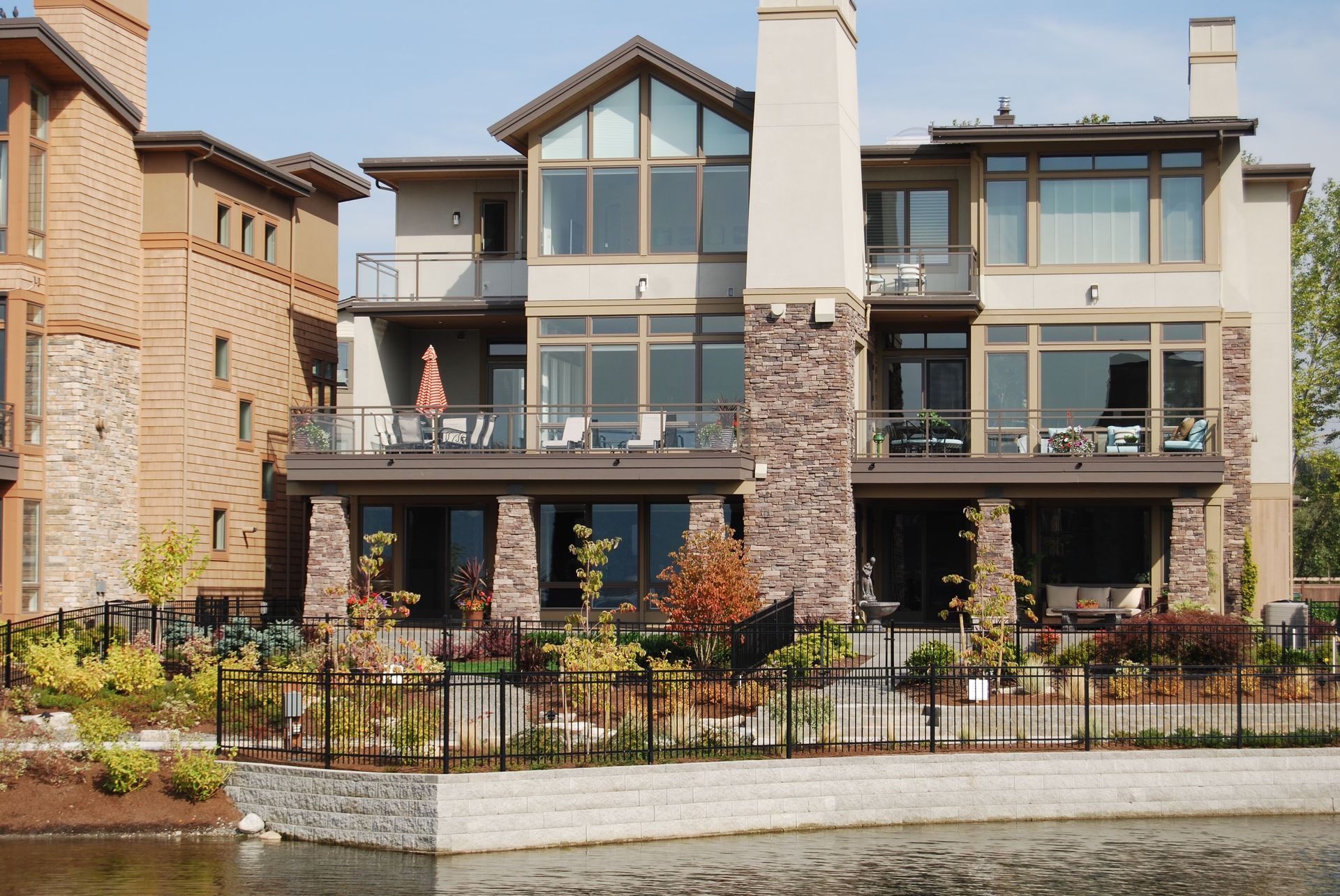 Row of modern waterfront townhomes with stone facades, balconies, and large windows along a calm canal