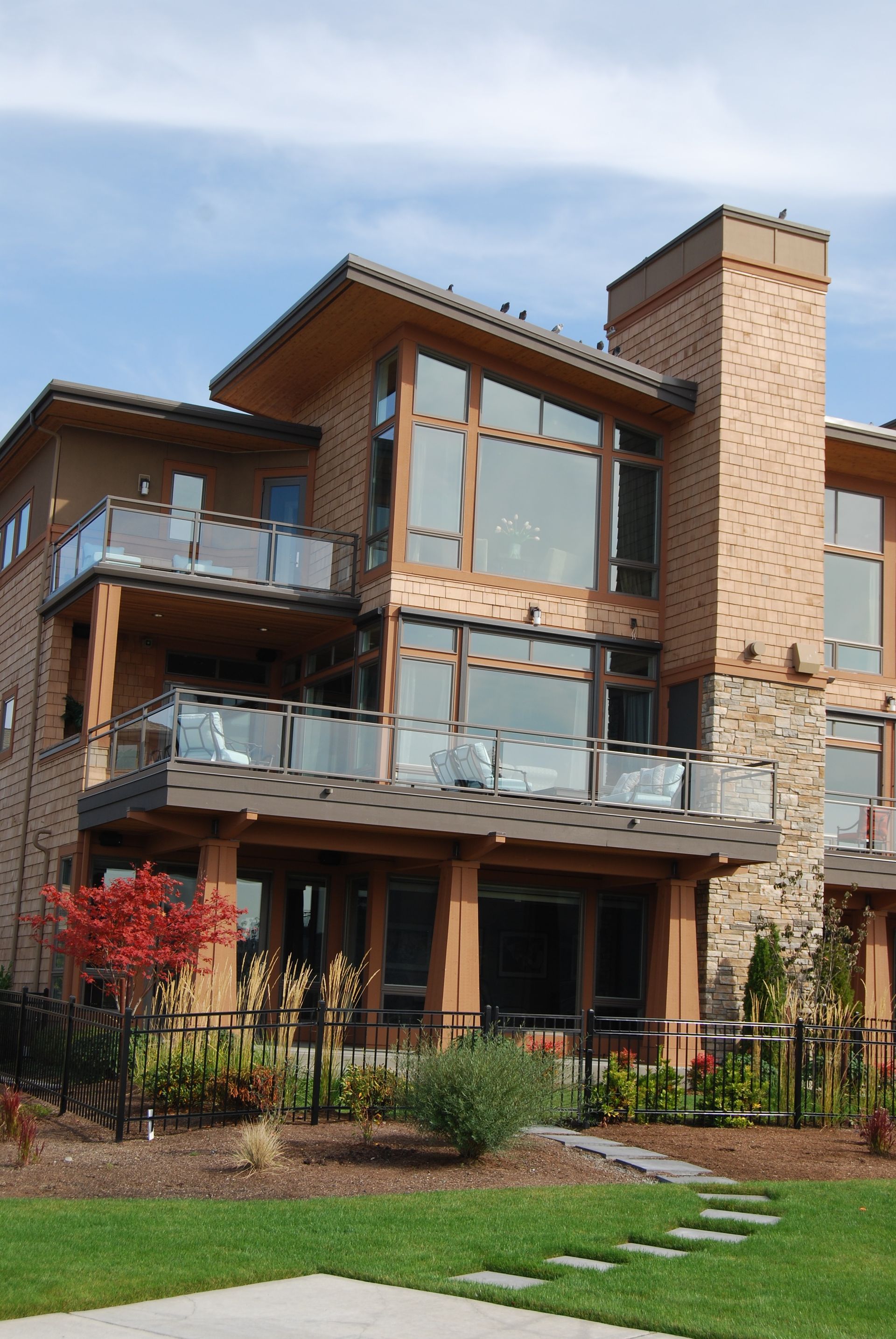 Modern multi-story brick and wood house with large windows, balconies, and a green lawn in front