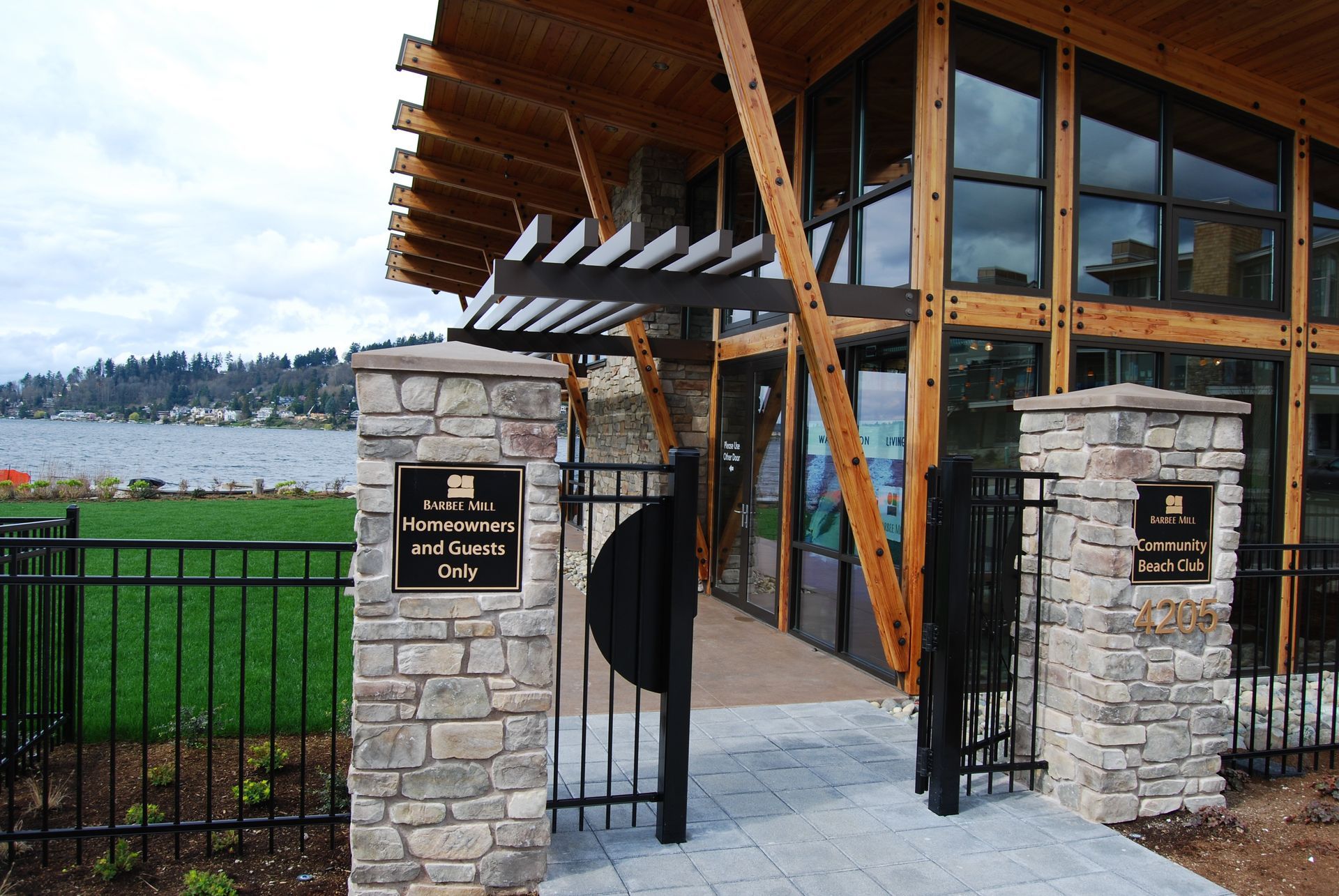 Stone entrance gate to a waterfront building with black iron gate and wooden roof, overlooking water and hillside