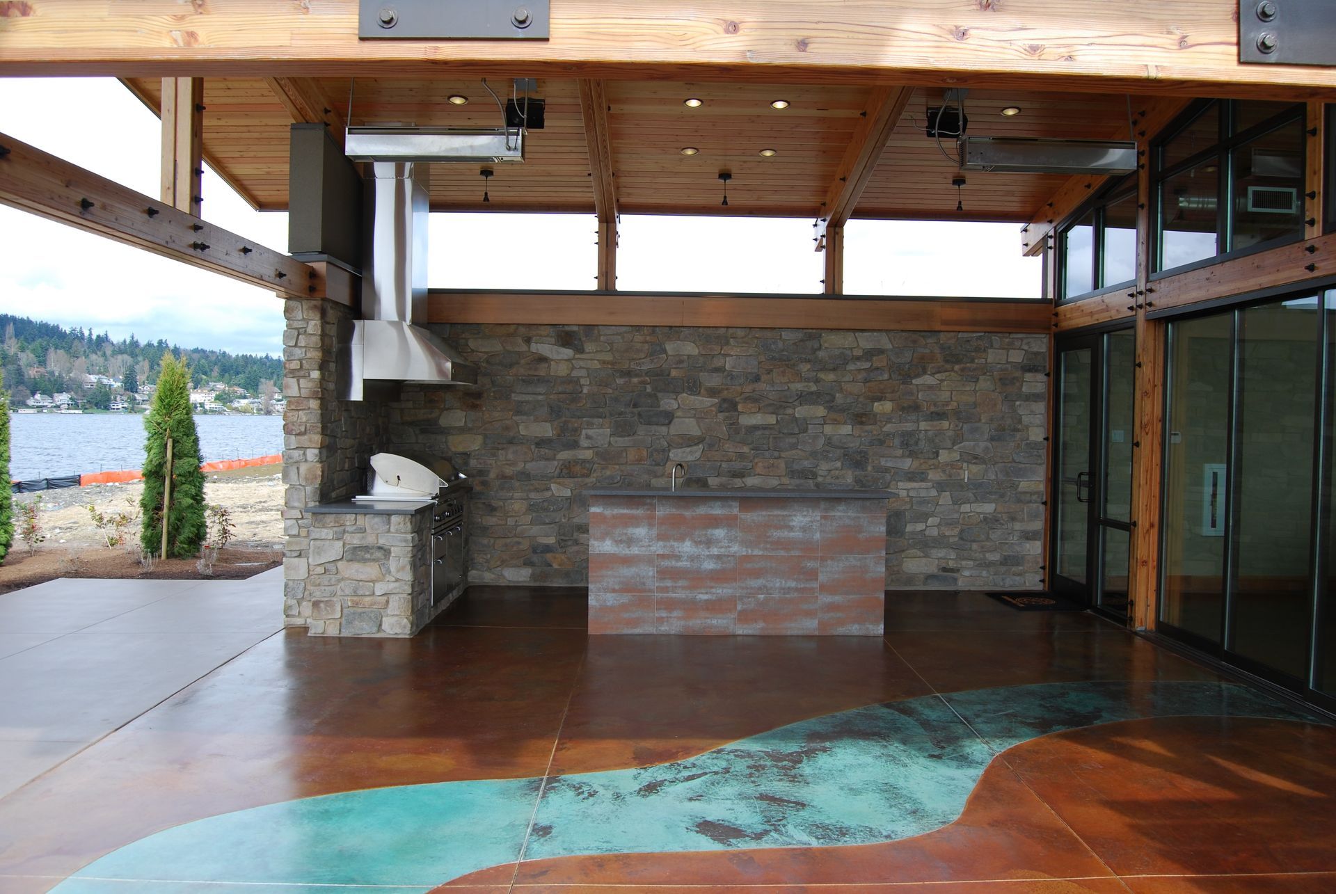 Modern open-air room with stone wall, wooden ceiling, and lake view through a side opening