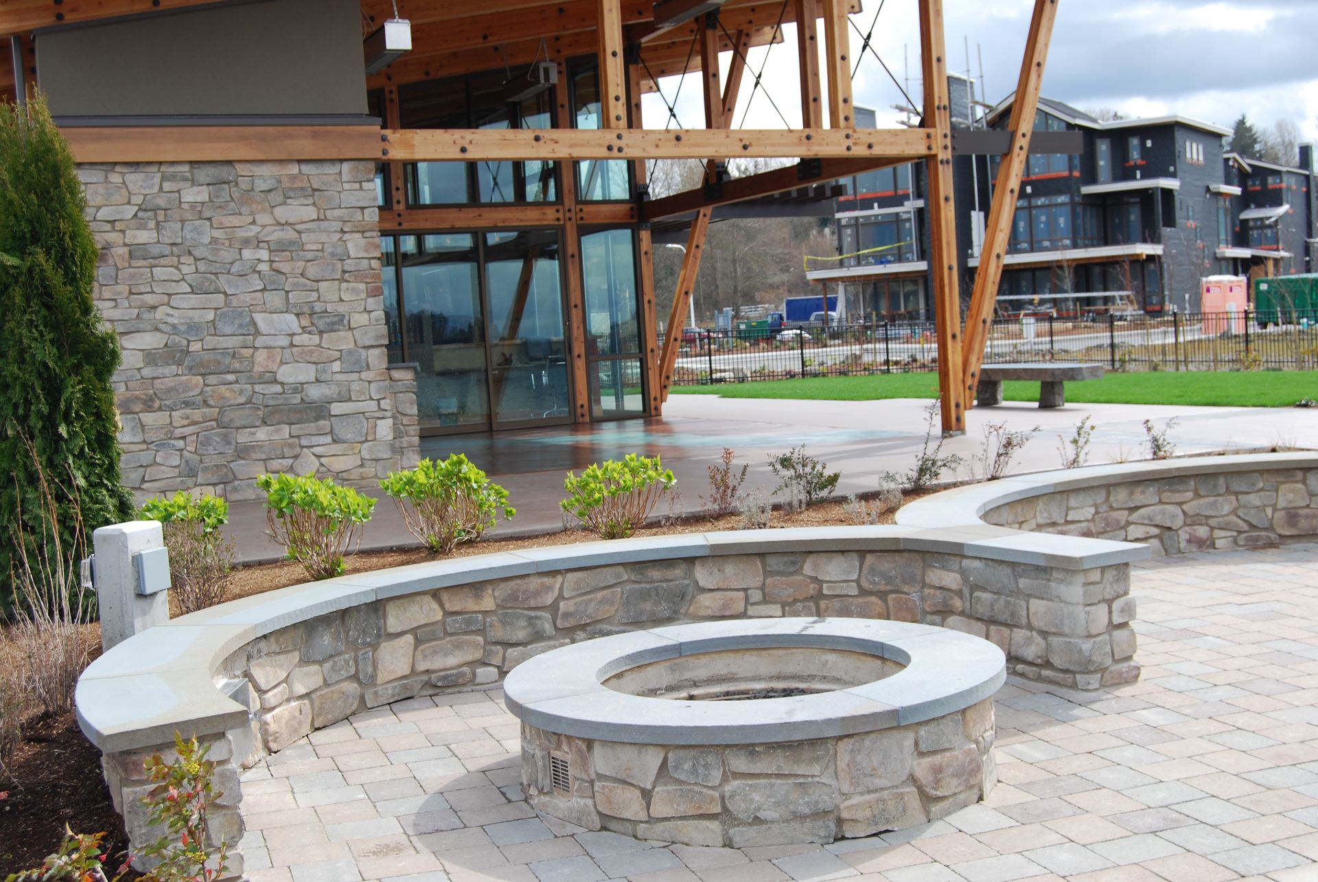 Stone courtyard seating area with circular fire pit and curved bench beside a modern building