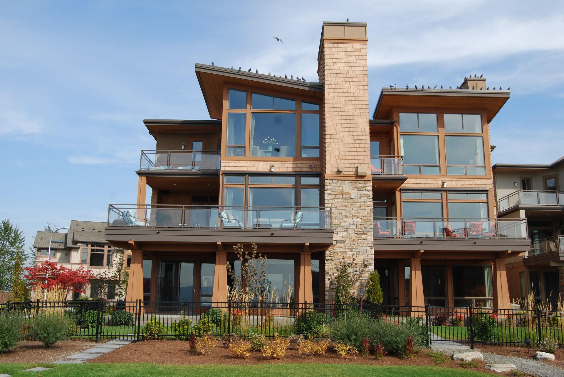 Modern multi-story house with wood and glass facade, balconies, and a stone chimney.