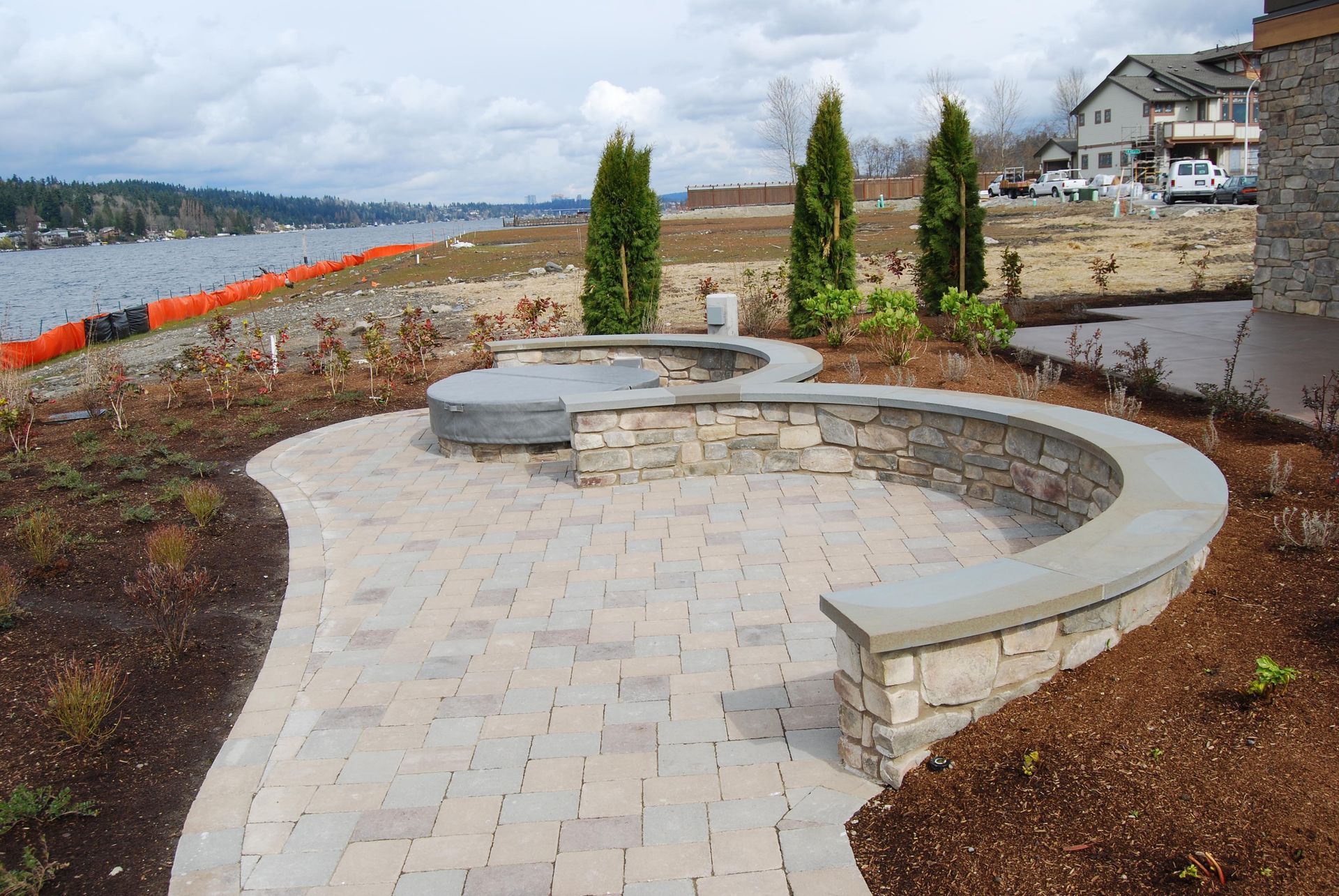 Curved stone bench and paved path in a landscaped waterfront park under cloudy skies