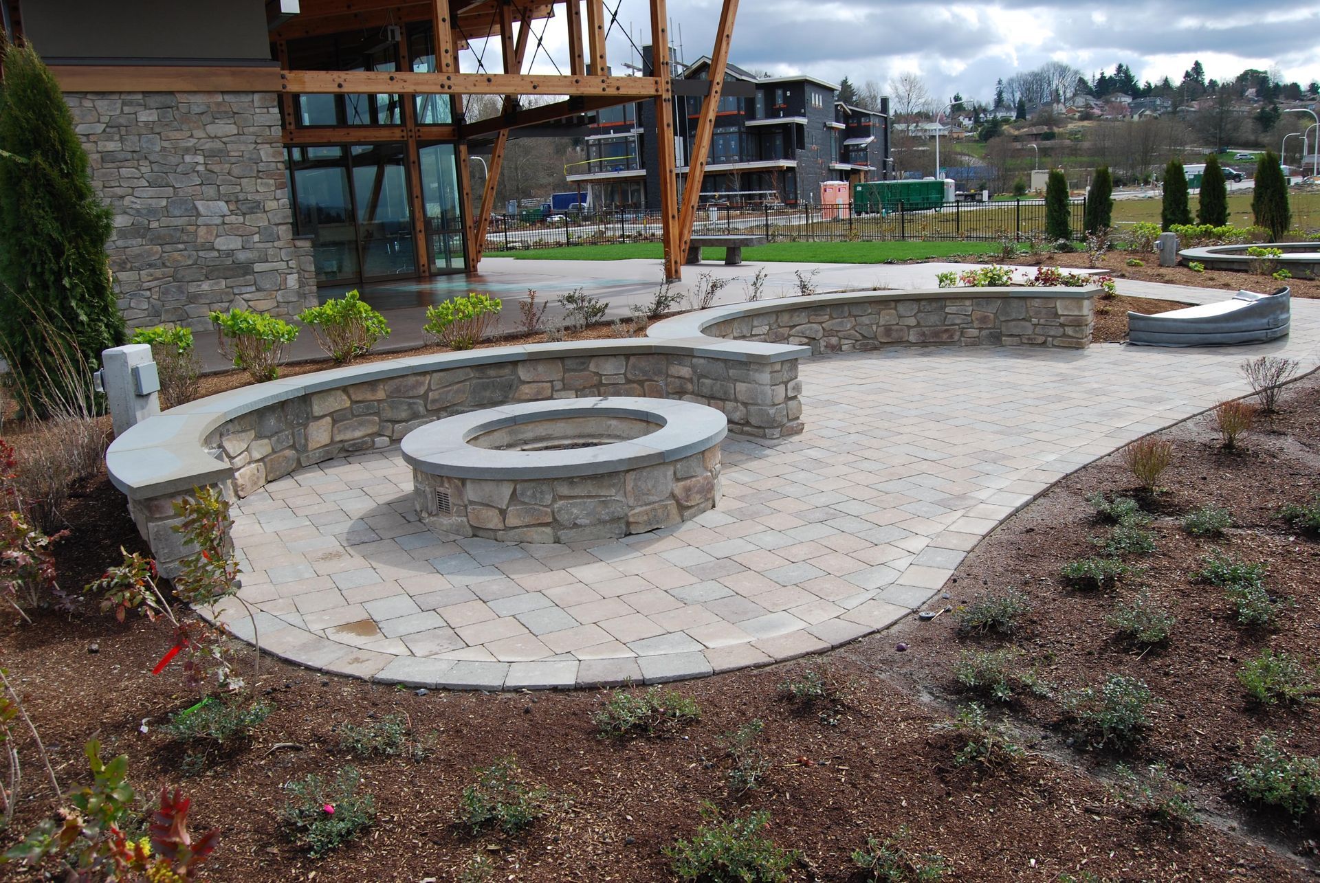 Curved stone outdoor seating area with circular benches and a fire pit in a landscaped courtyard