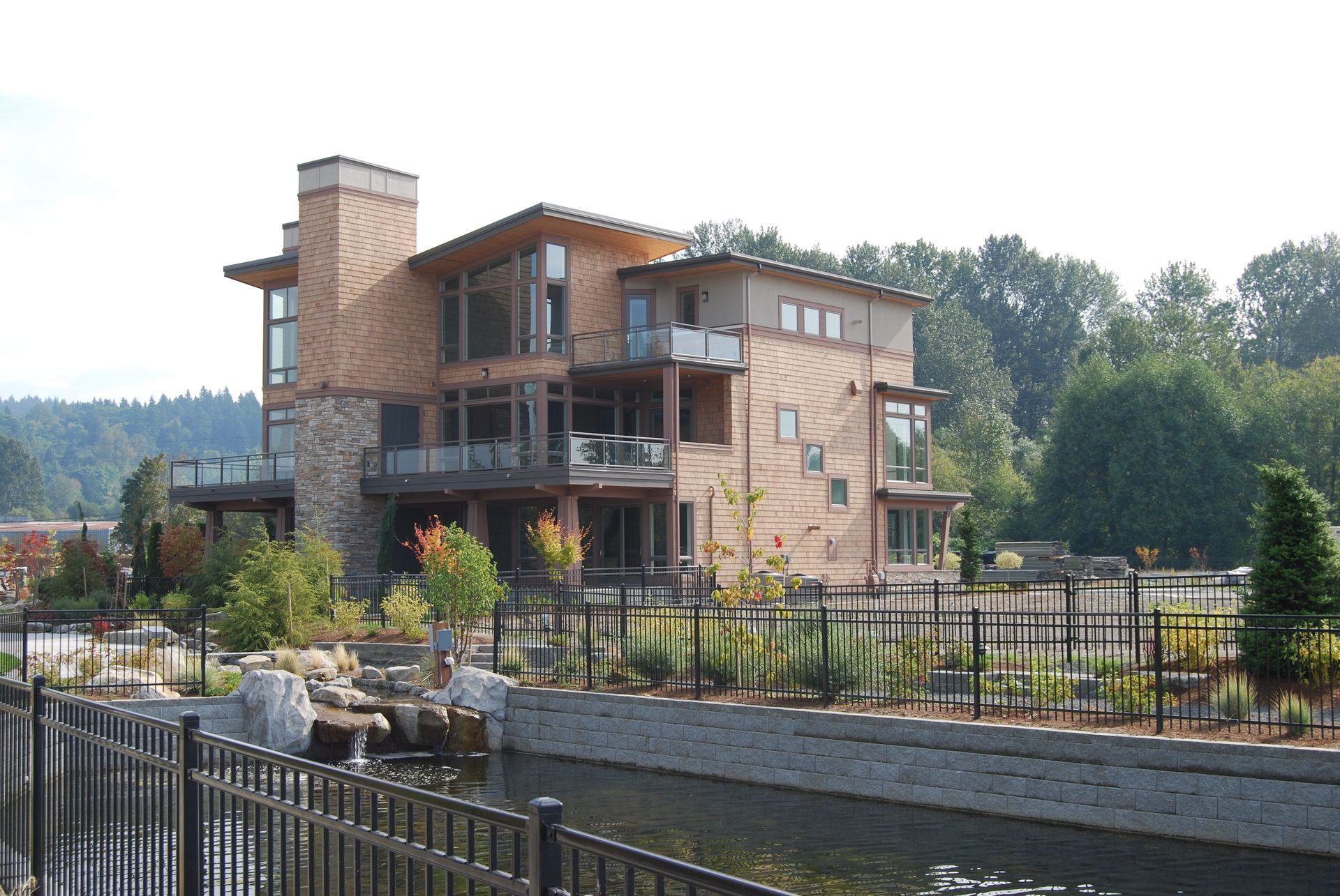 Modern stone-and-wood house with a tower beside a canal and black metal fence.