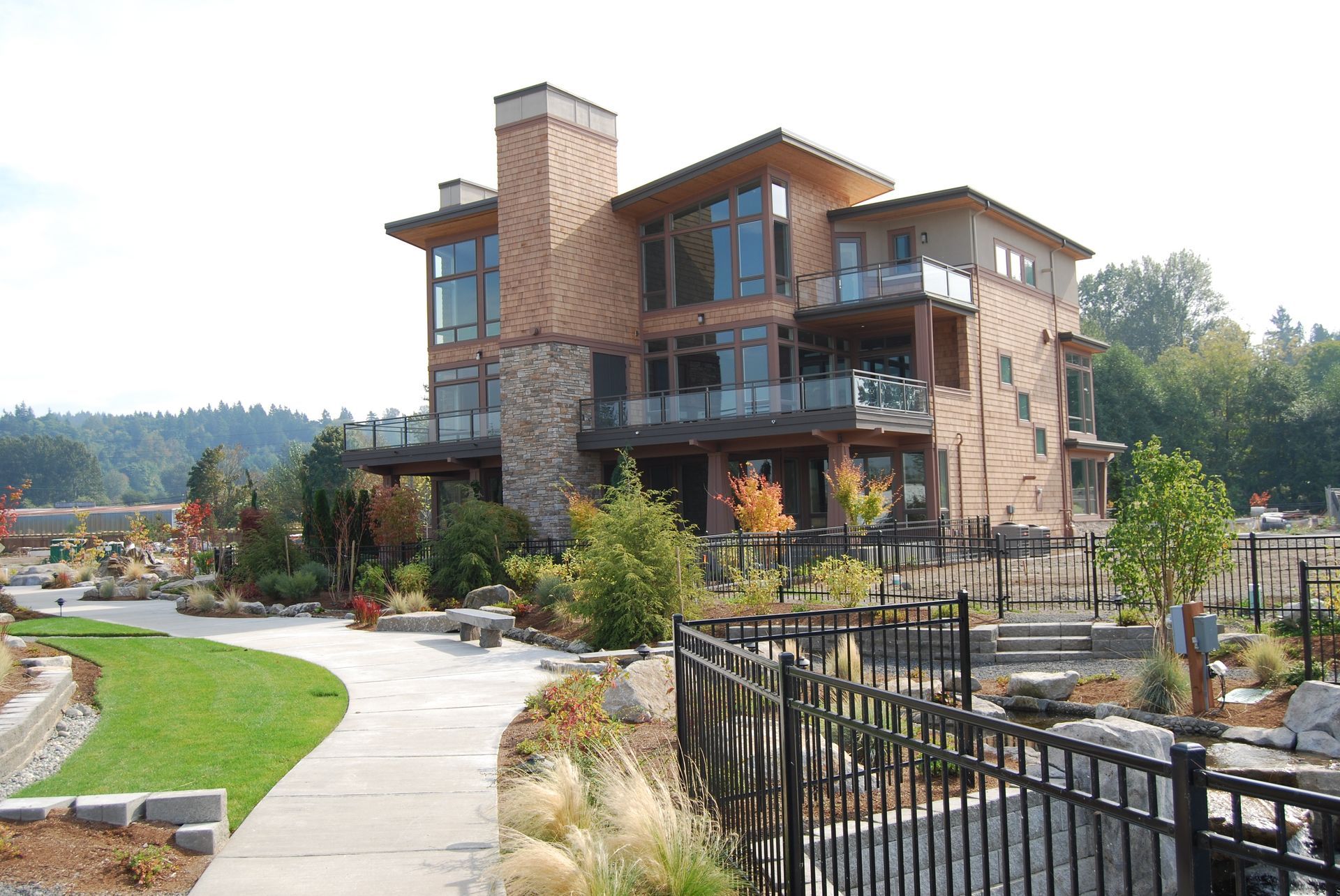 Modern multi-story lodge with stone and wood exterior beside a landscaped path and fence.