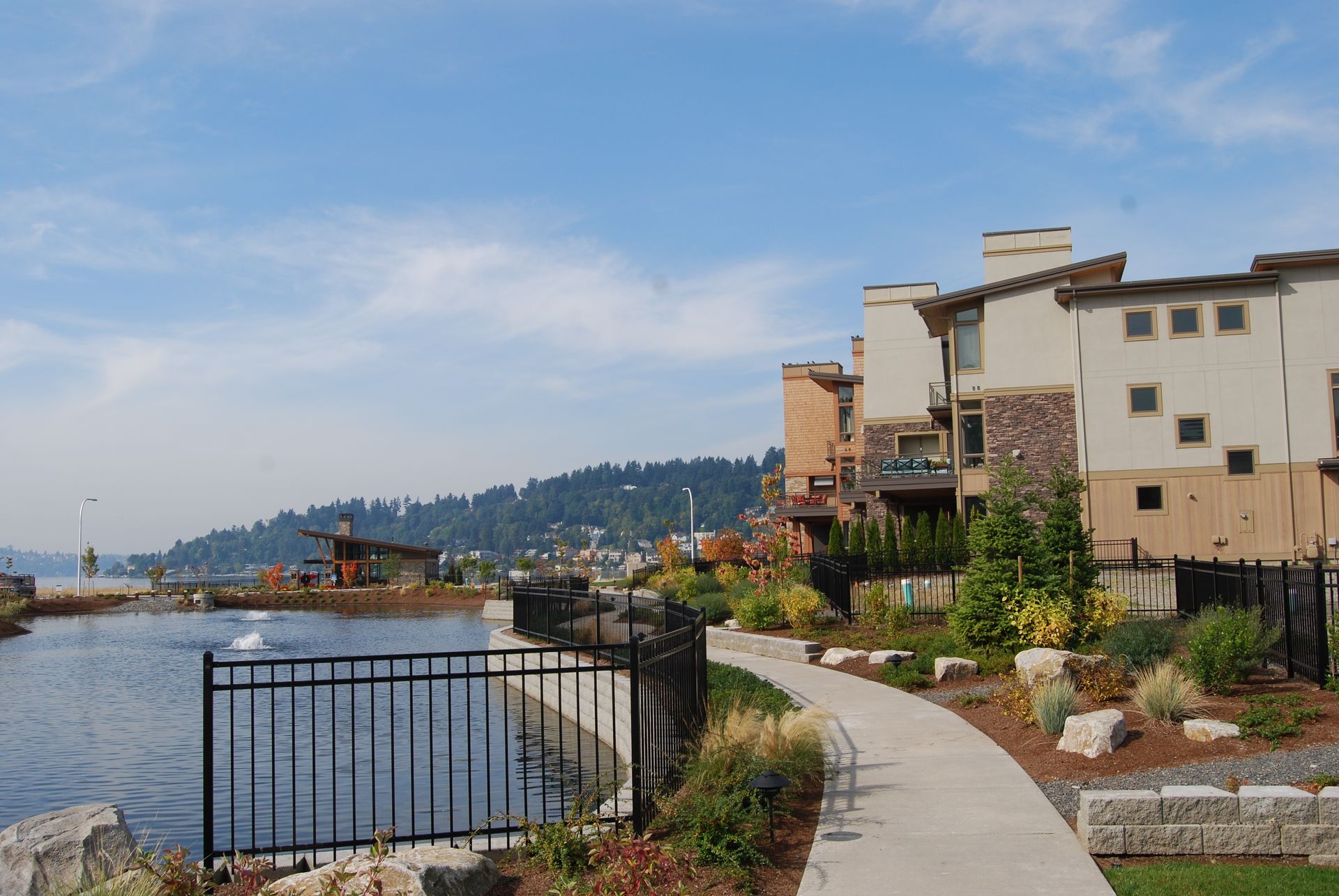 Curved waterfront path beside metal railing, calm bay, and pastel buildings under a blue sky