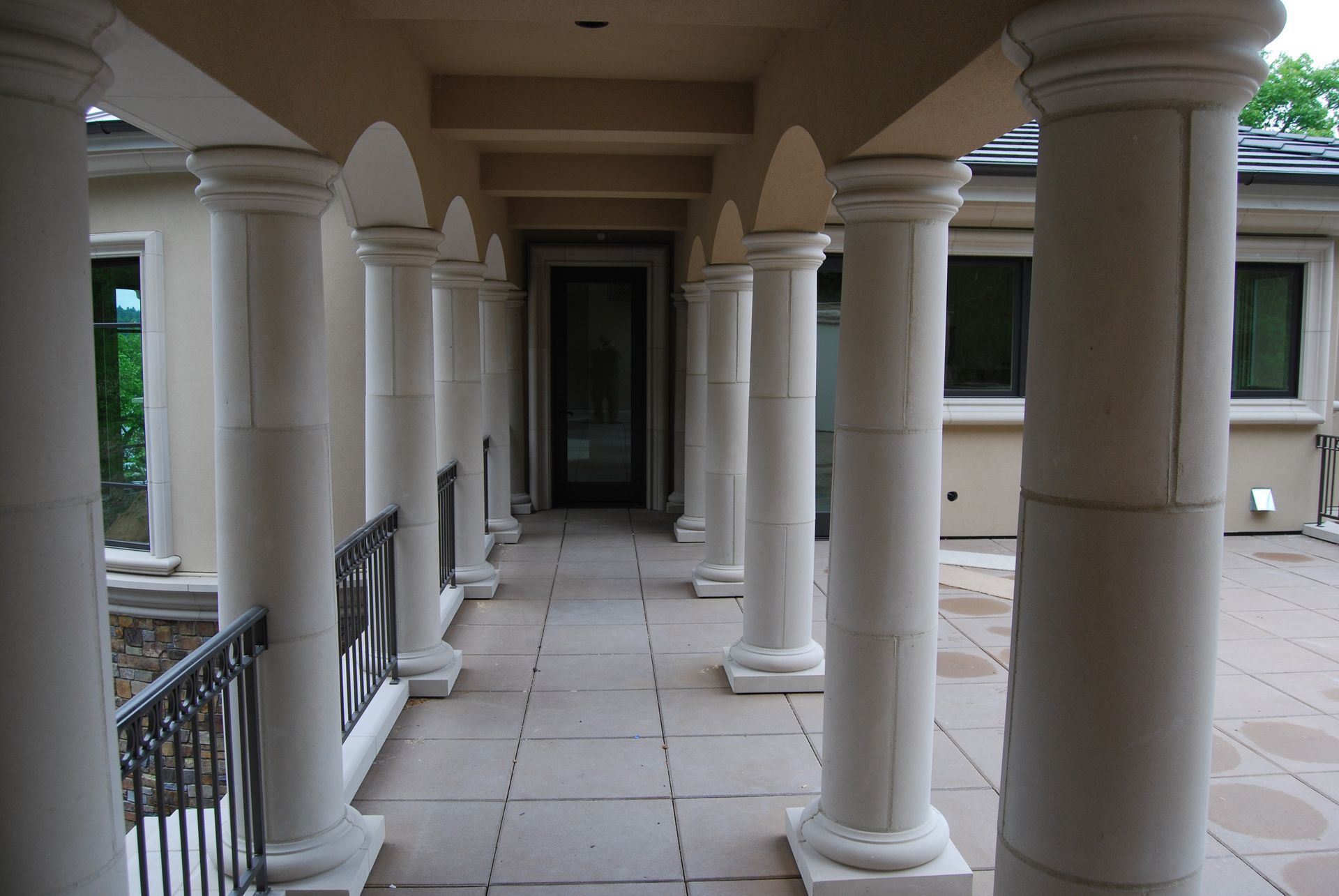 Covered stone walkway with white columns and arched ceiling leading to a doorway