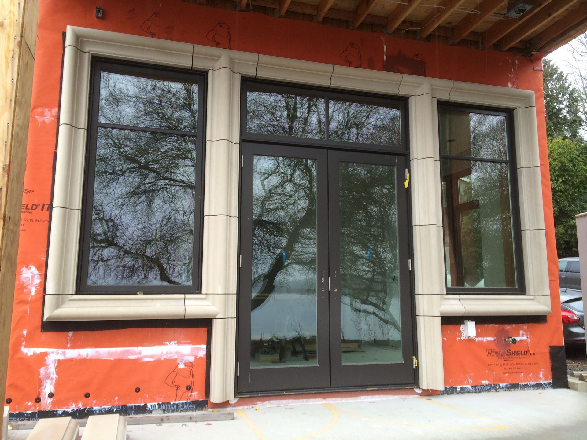 Front view of a small building with orange walls, large windows, and a glass door under a wooden roof overhang