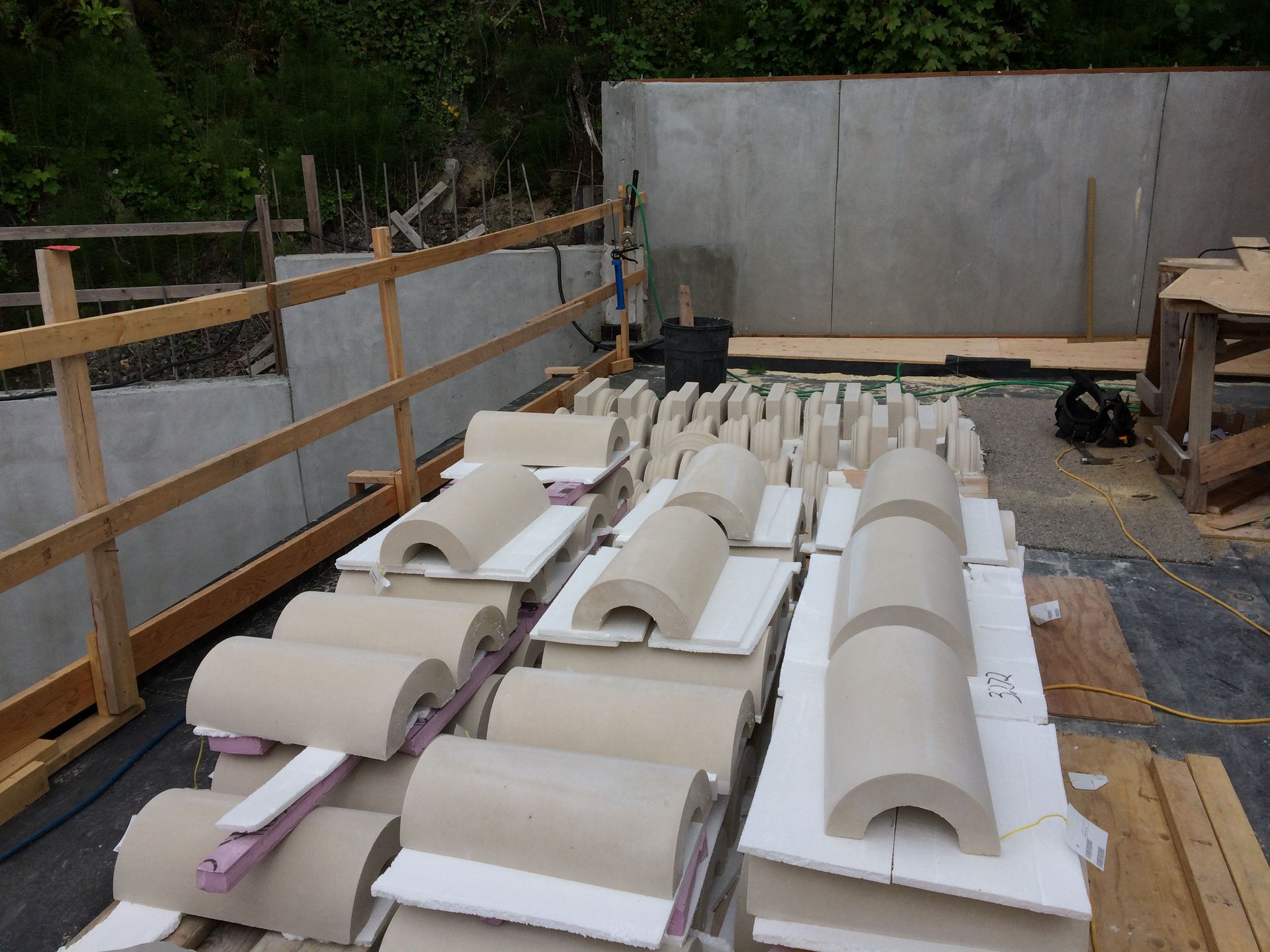 Stacks of white curved roofing panels on a wooden pallet in an outdoor construction area.