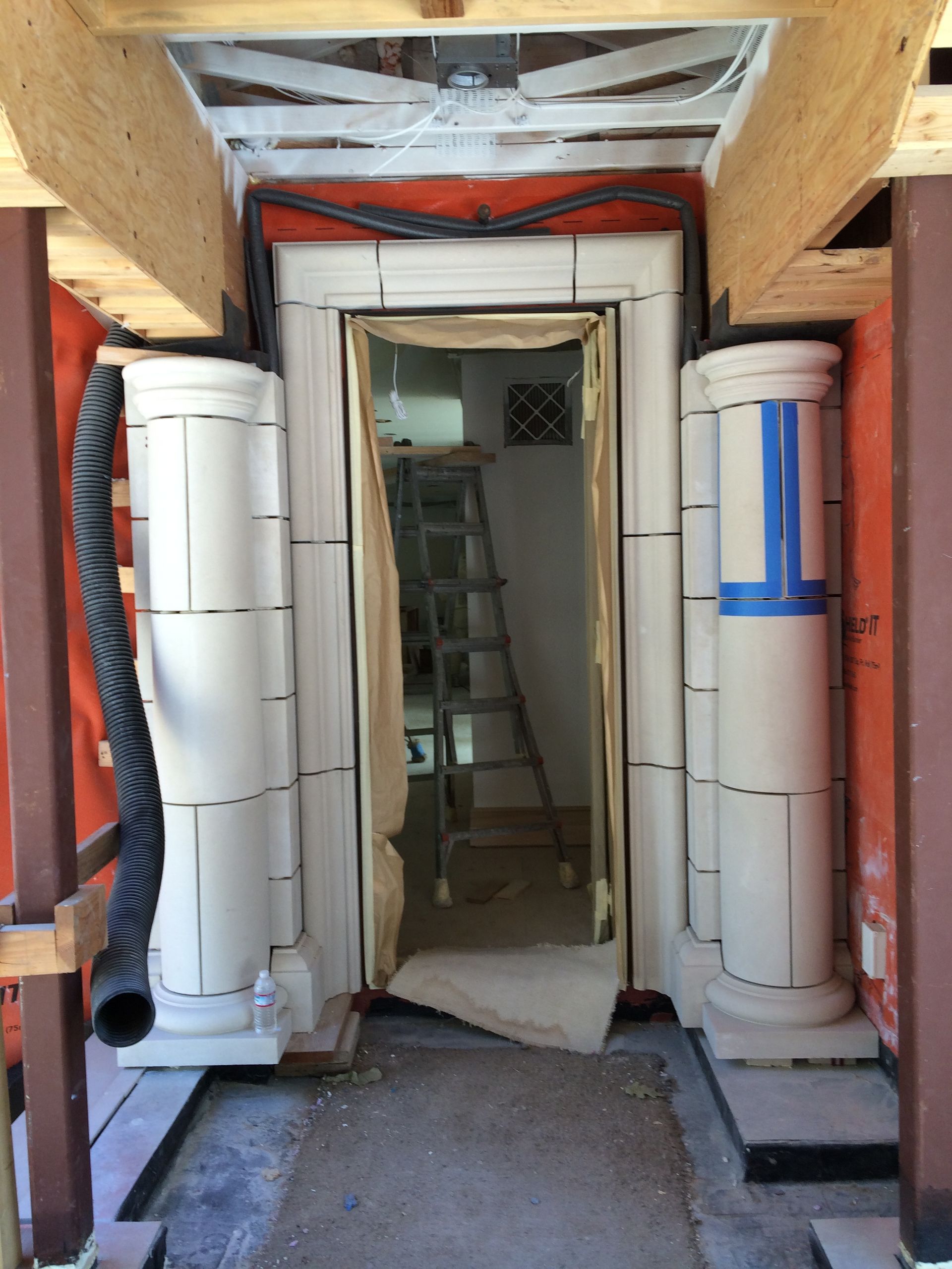 Construction corridor with two white cylindrical forms flanking a doorway and ladder inside