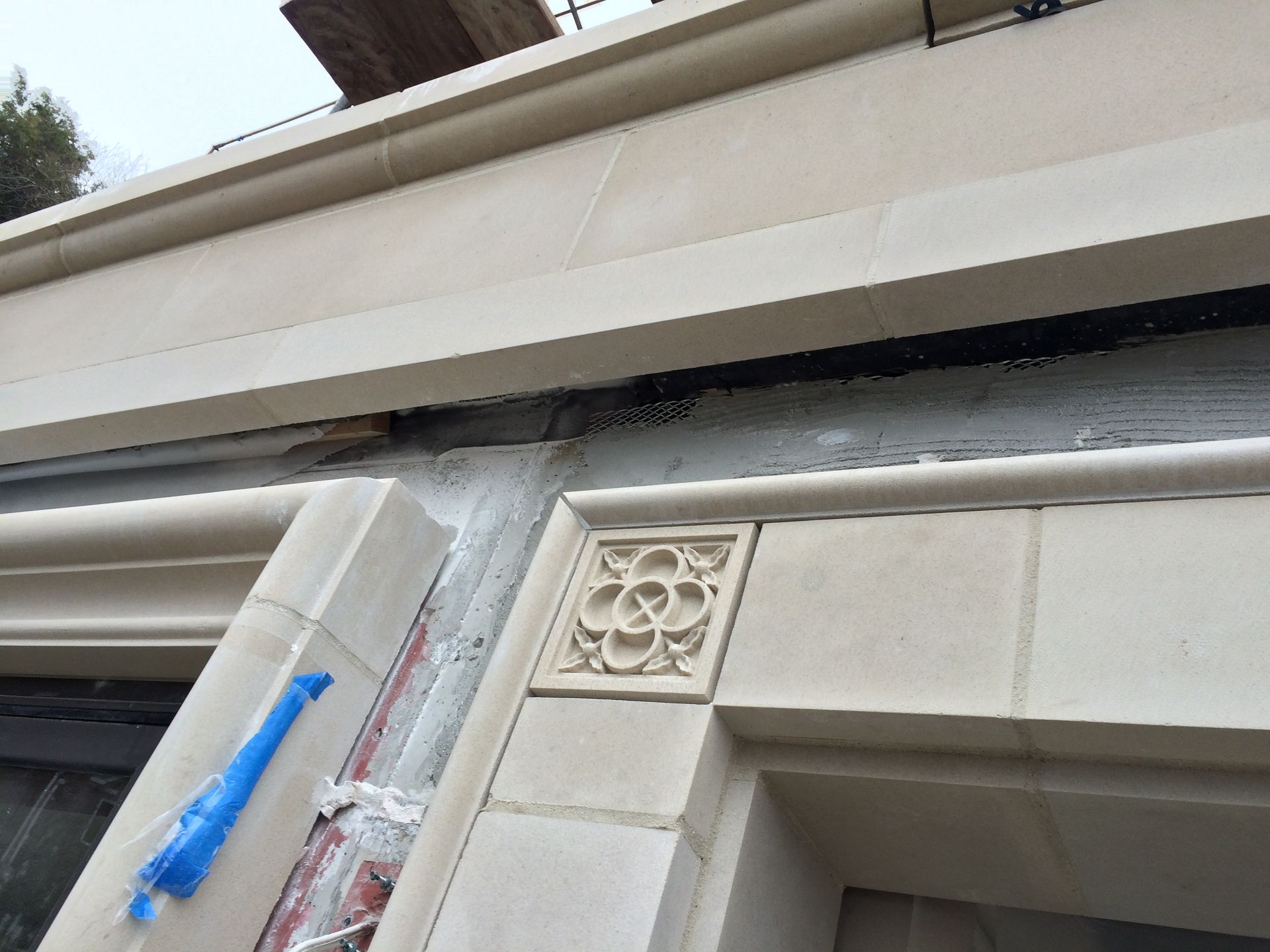 Close-up of a building facade with decorative trim and a blue repair tool taped to the wall