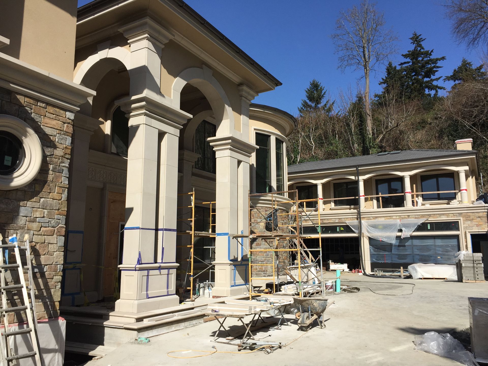 Mansion under construction with scaffolding, columns, and unfinished stone exterior in bright sunlight