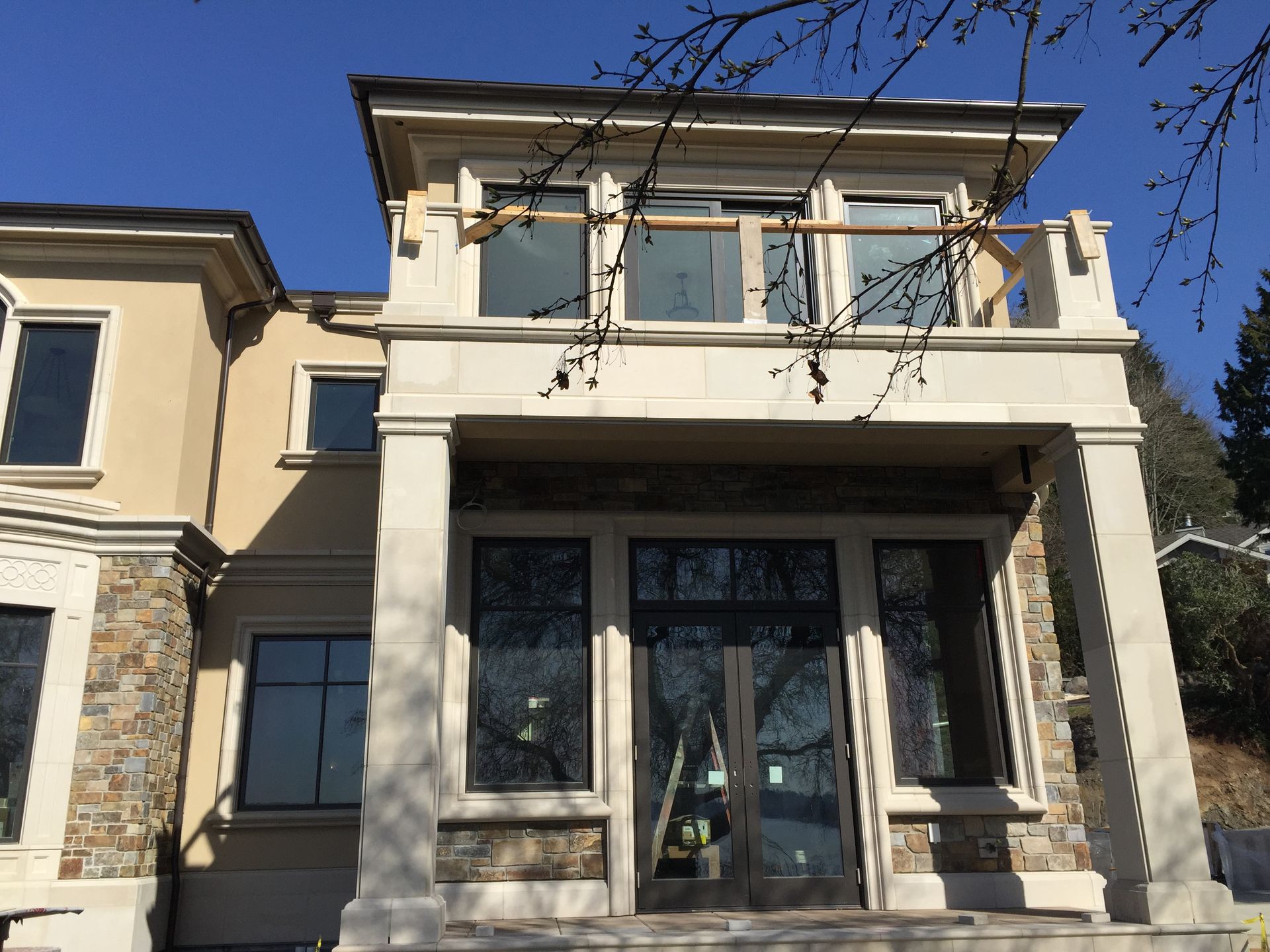 Front view of a modern beige house with large windows and a balcony under a clear blue sky