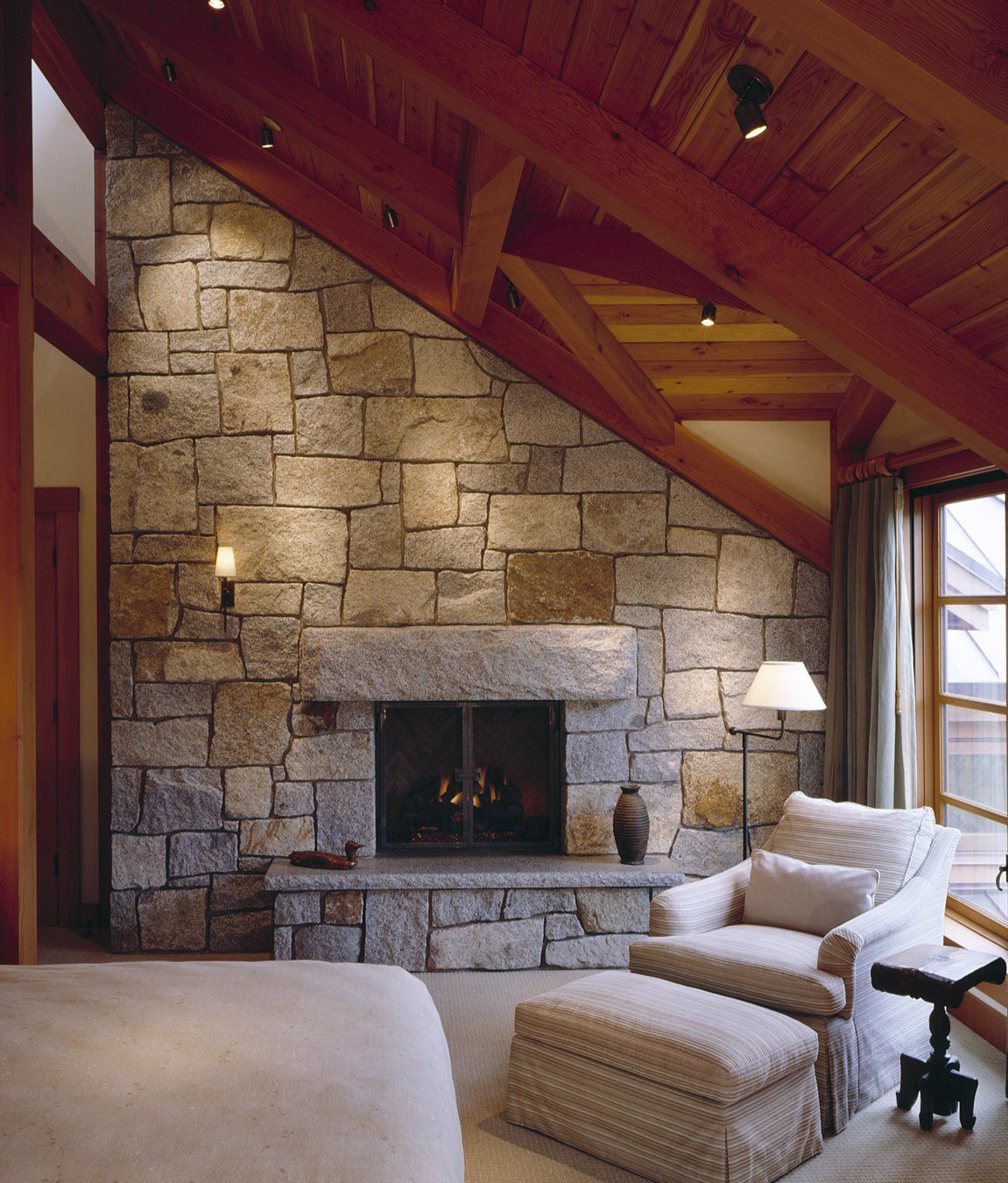 Cozy living room with stone fireplace, wood-beamed ceiling, beige seating, and windows with natural light