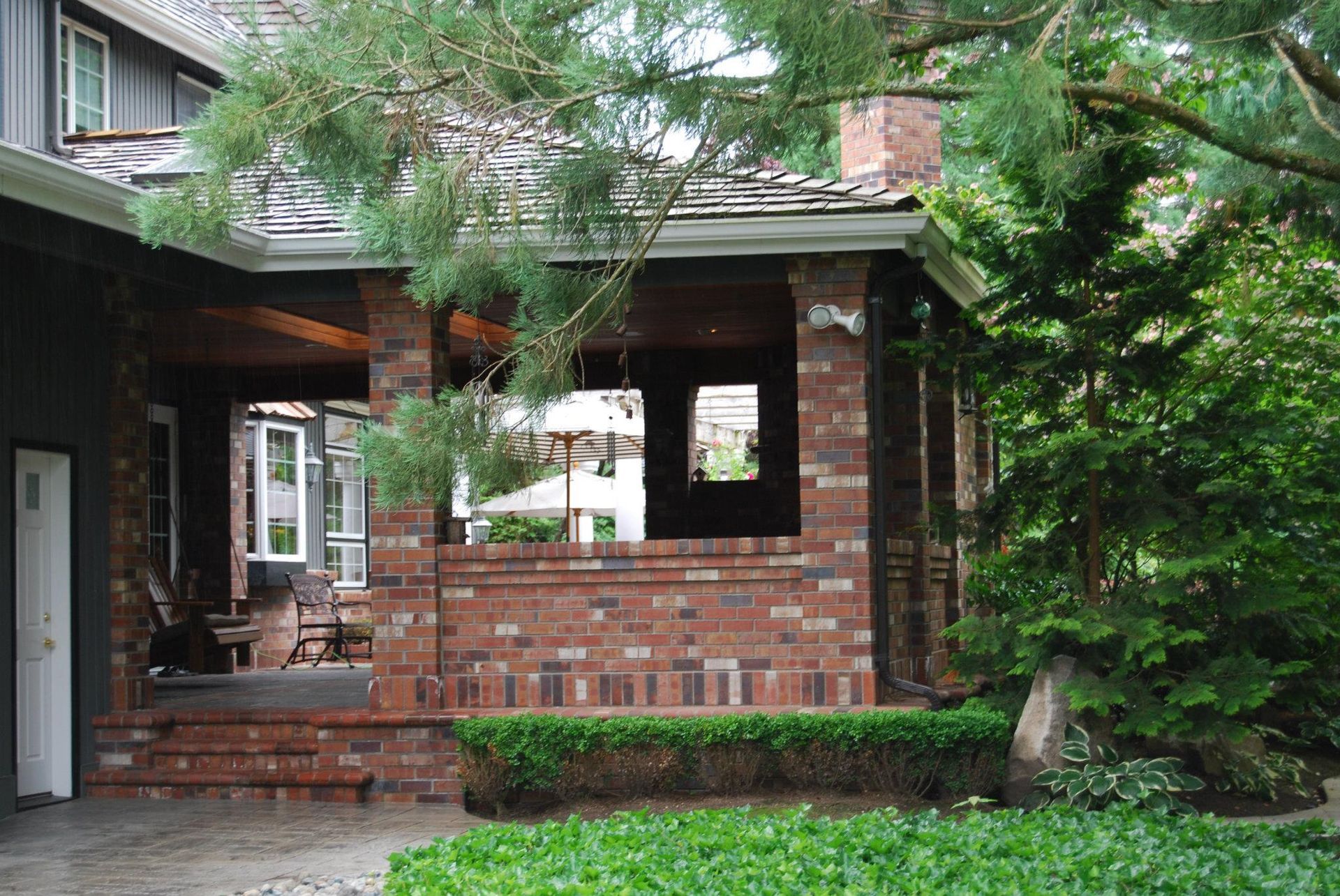 Brick house front porch with steps, large window, and green trees in the yard
