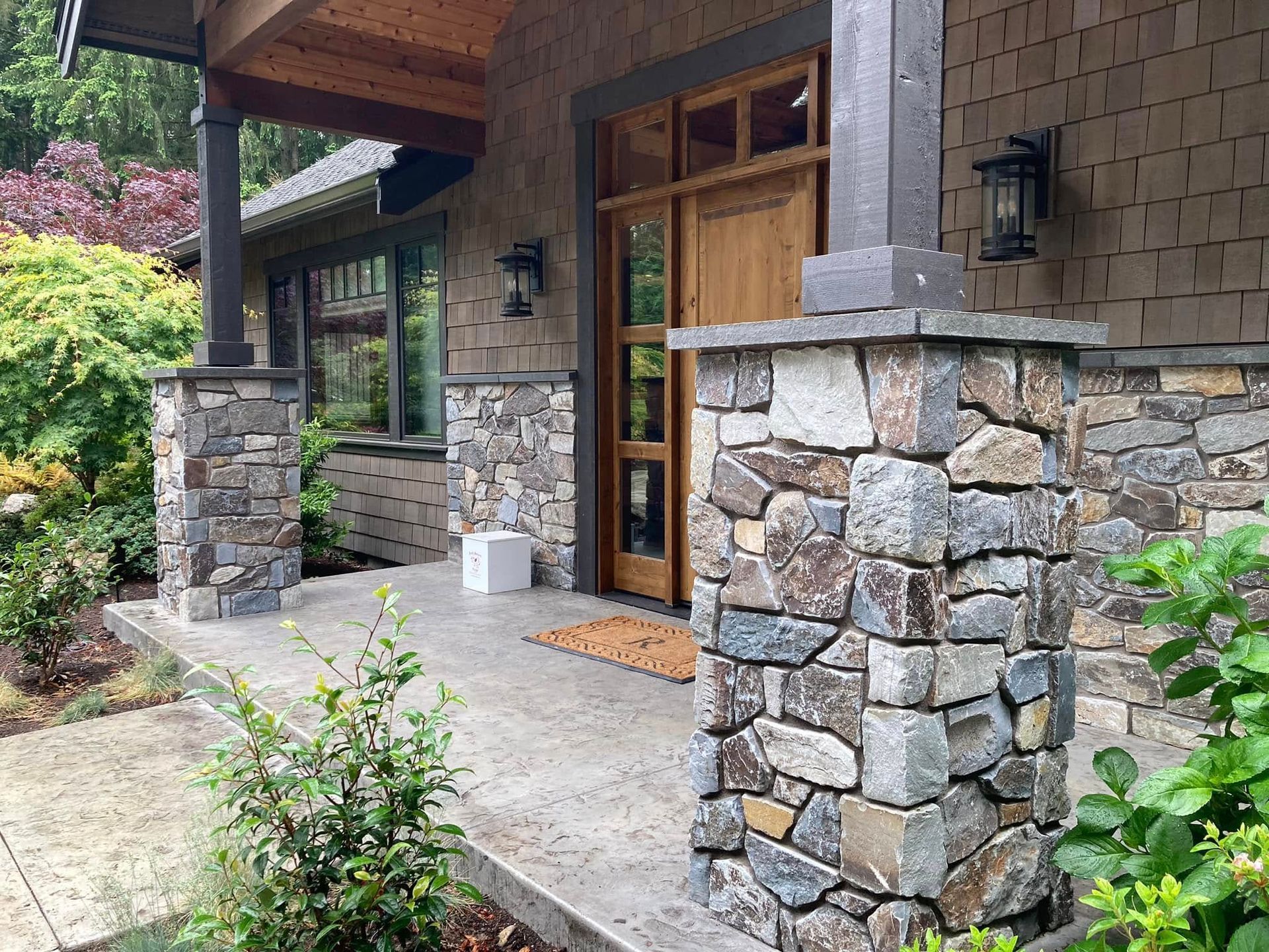 Stone front porch with wood doors, stone columns, and potted plants at a rustic house entrance