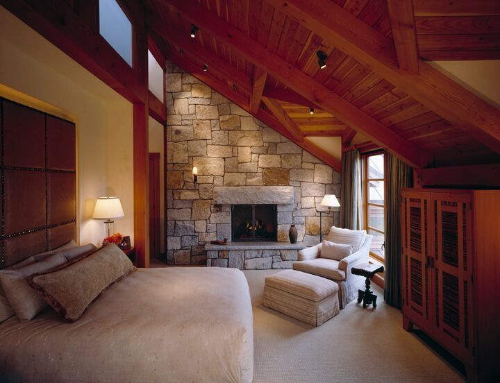 Cozy rustic bedroom with stone fireplace, wood beams, and warm red accents