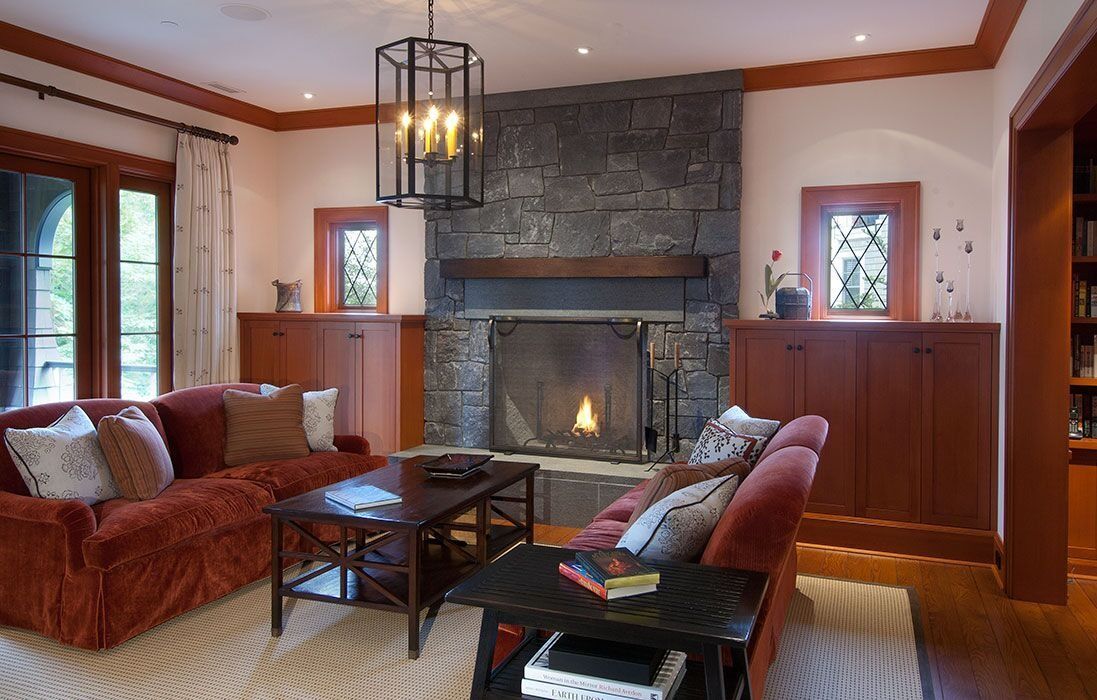 Cozy living room with stone fireplace, red sofas, dark wood trim, and a hanging lantern pendant light.