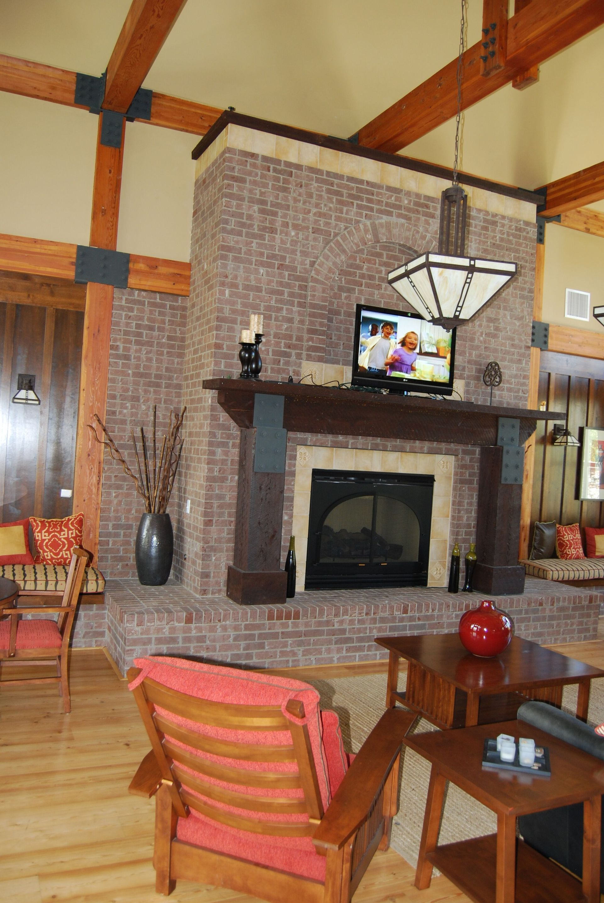Cozy lodge living room with brick fireplace, wood beams, red chairs, and a TV above the mantel