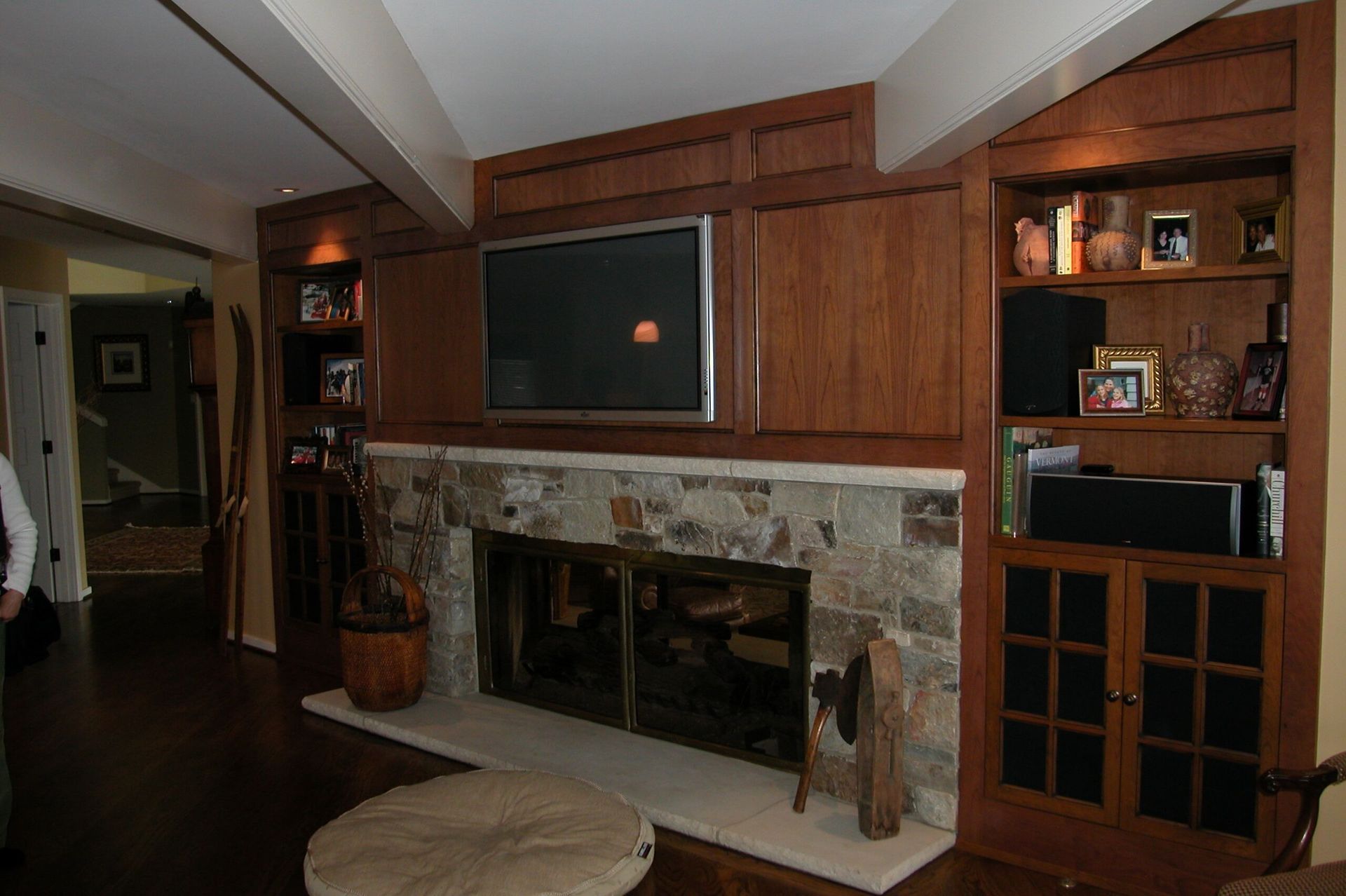 Cozy living room with stone fireplace, wood paneling, built-in shelves, and a large TV above the mantel.