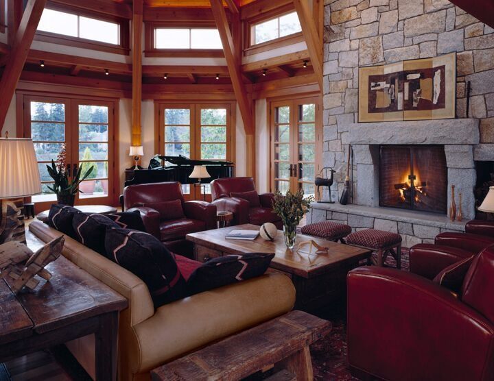 Luxury living room with stone fireplace, large windows, leather chairs, and a person lounging on a sofa