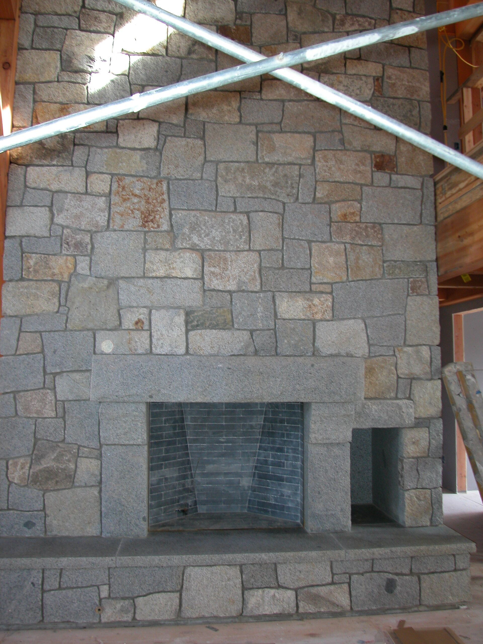 Stone fireplace with a dark firebox and metal beams overhead in an unfinished room