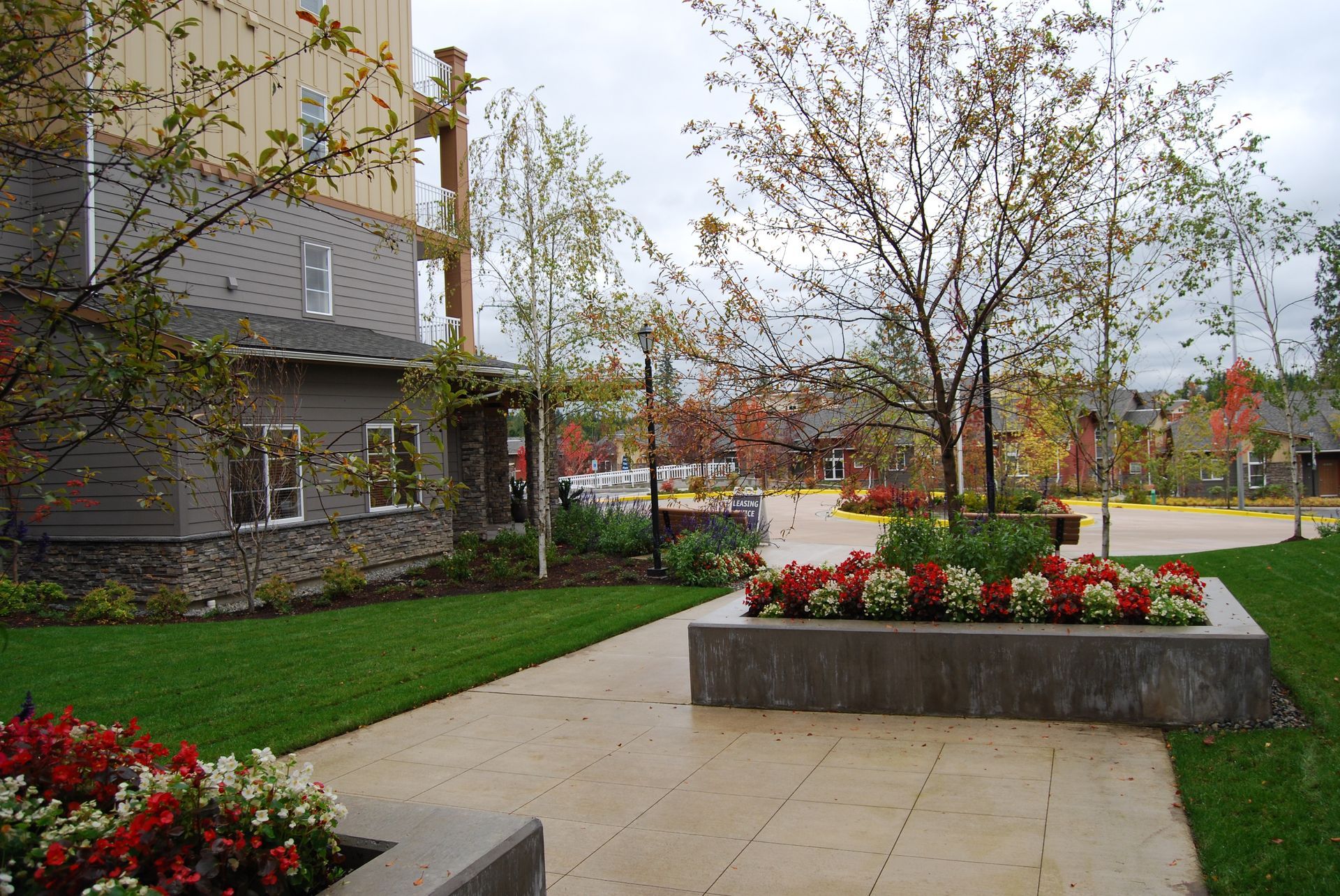 Landscaped courtyard with flower beds, green lawn, and a paved walkway beside an apartment building.