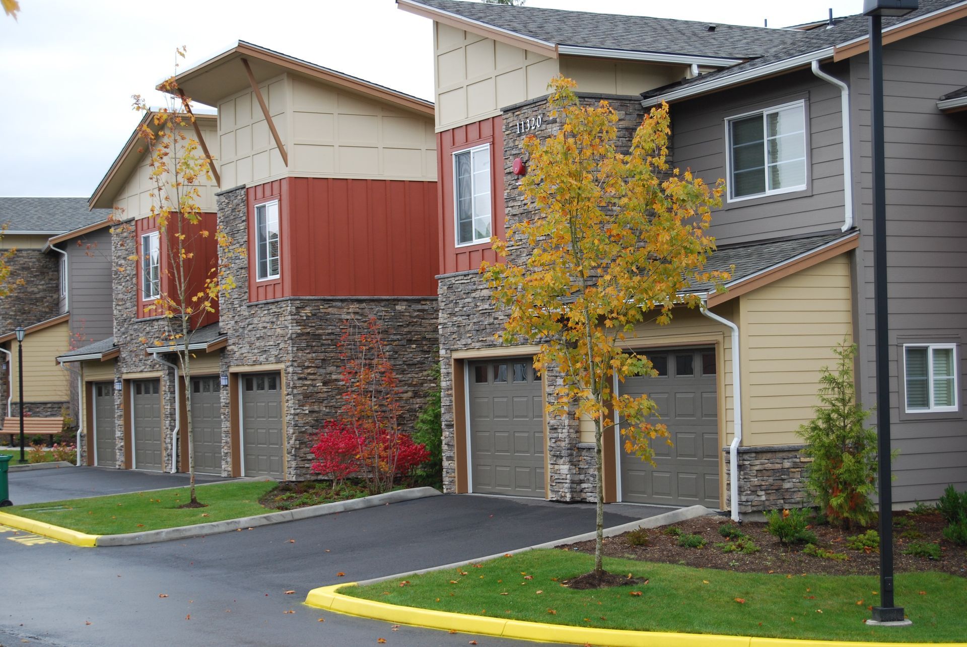 Row of modern townhouses with garages, gray siding, and autumn trees along a wet street