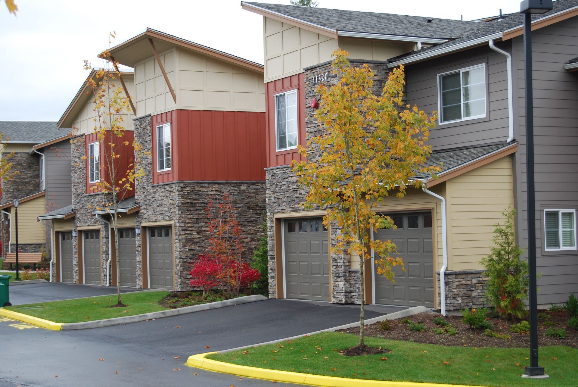 Row of modern townhouses with garages, autumn trees, and wet driveways in a residential complex