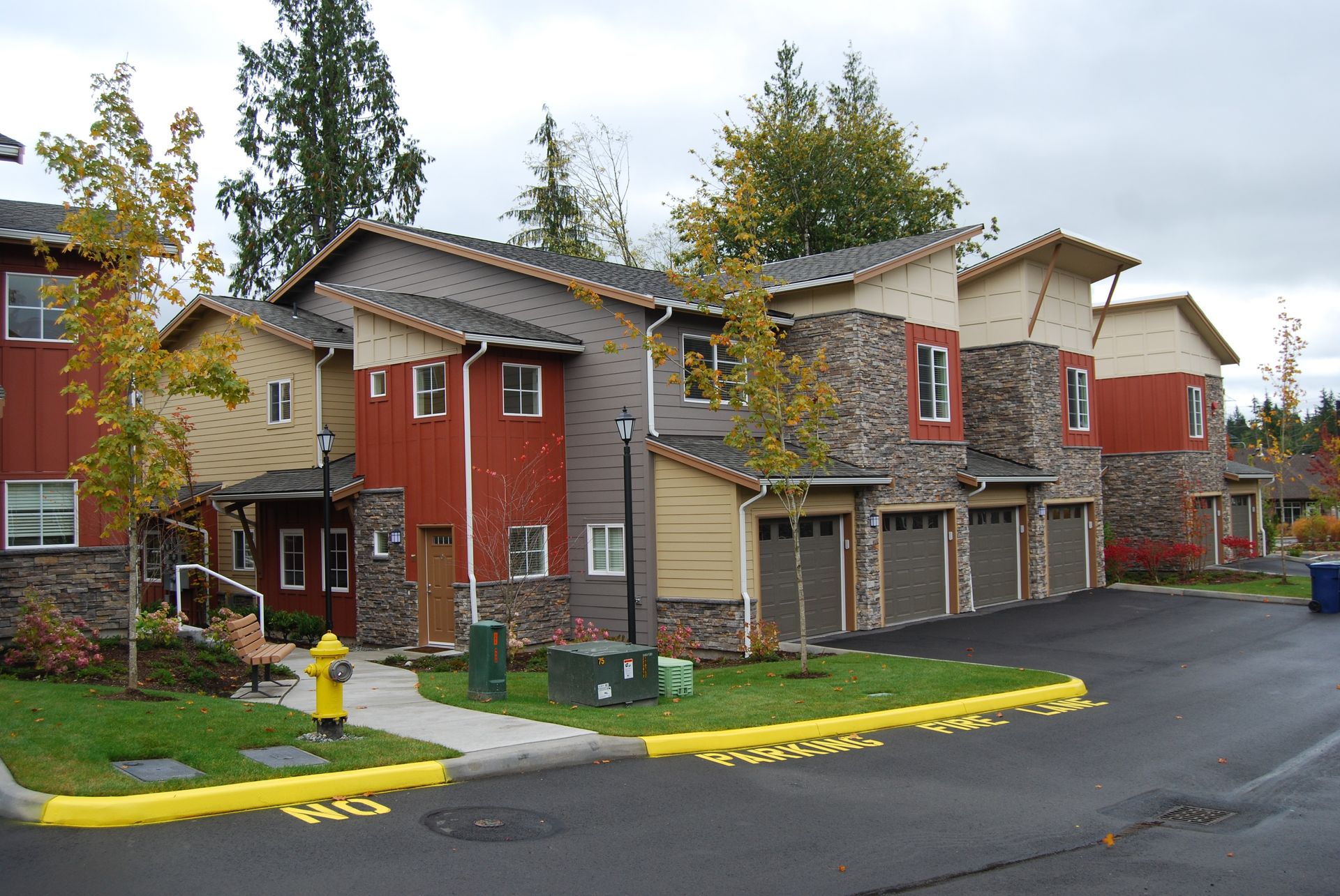 Apartment and townhouse complex with red siding, garages, and yellow curb markings in a parking lot