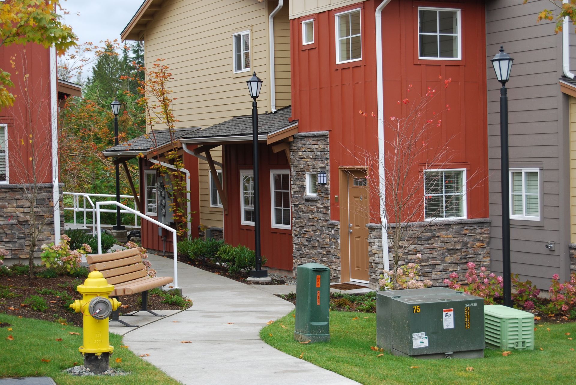 A curved sidewalk beside red and tan townhouses, with a yellow fire hydrant and green utility boxes.