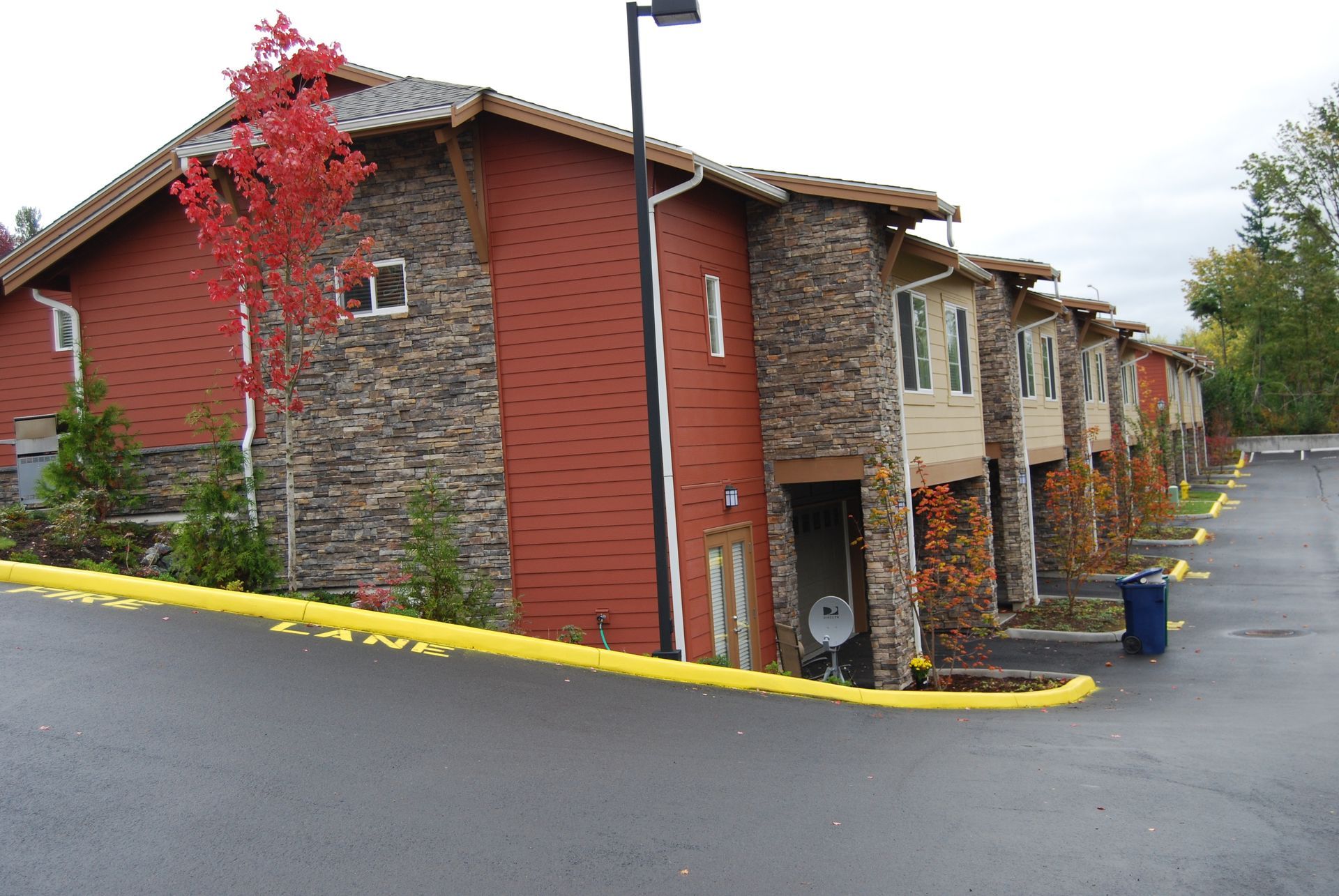 Apartment building corner with red brick and stone siding, yellow curb, and a wet paved driveway