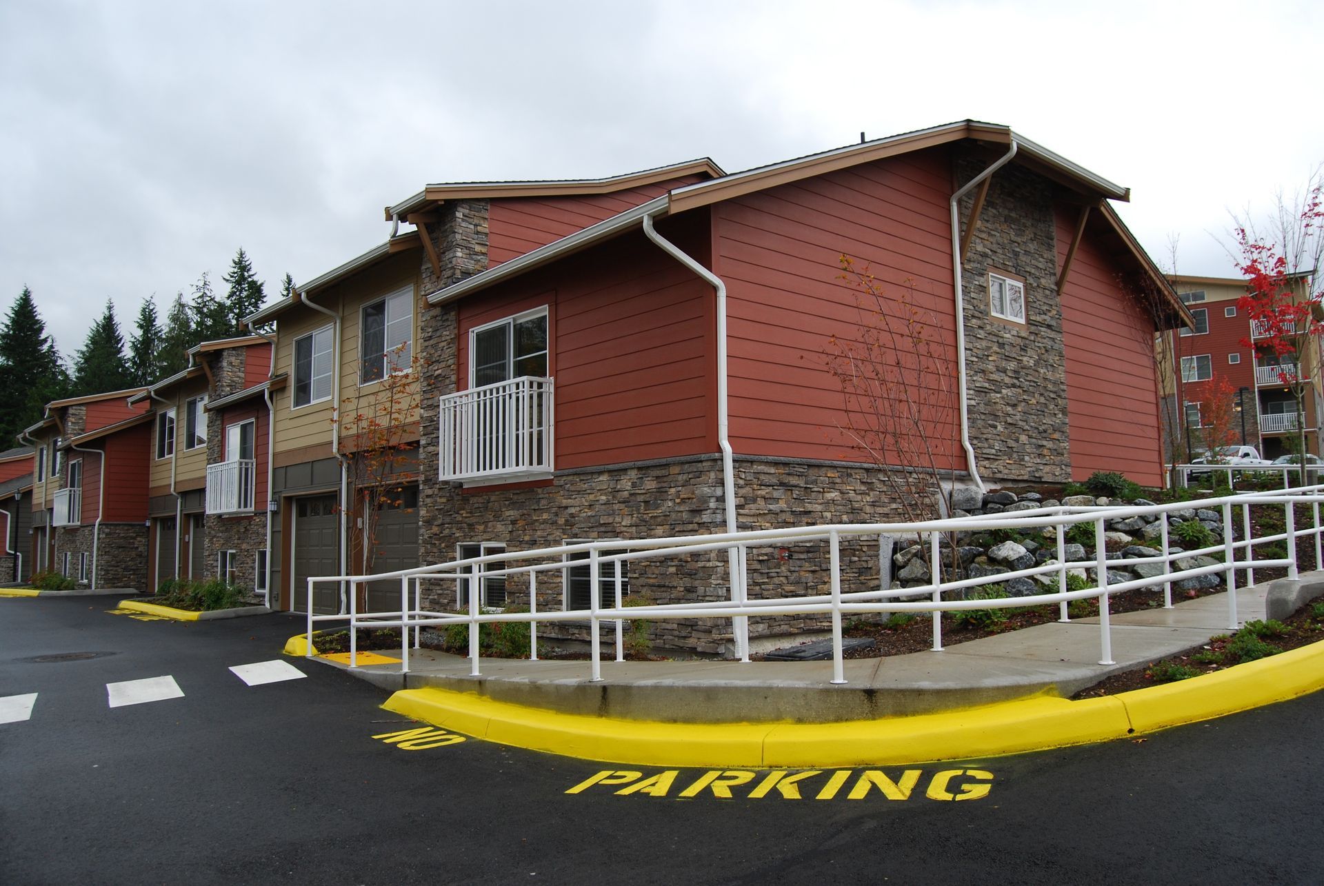 Brick apartment building with red siding, white railings, and yellow parking curb on a wet street