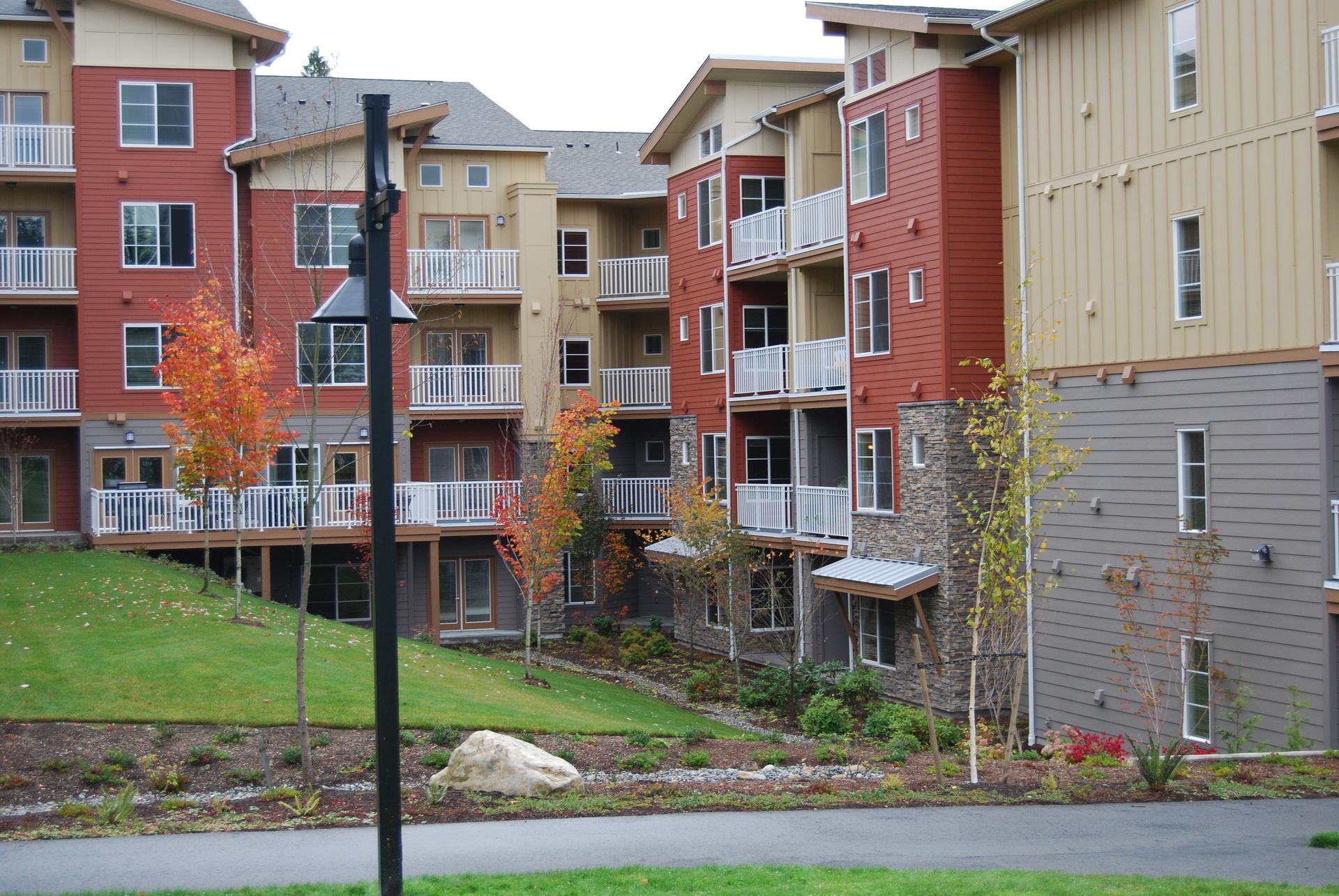 Apartment buildings with balconies beside a grassy courtyard and sidewalk under overcast skies