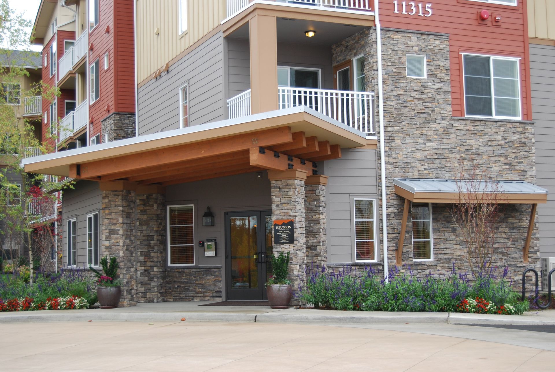 Apartment building entrance with stone and brick exterior, covered awning, and balconies above
