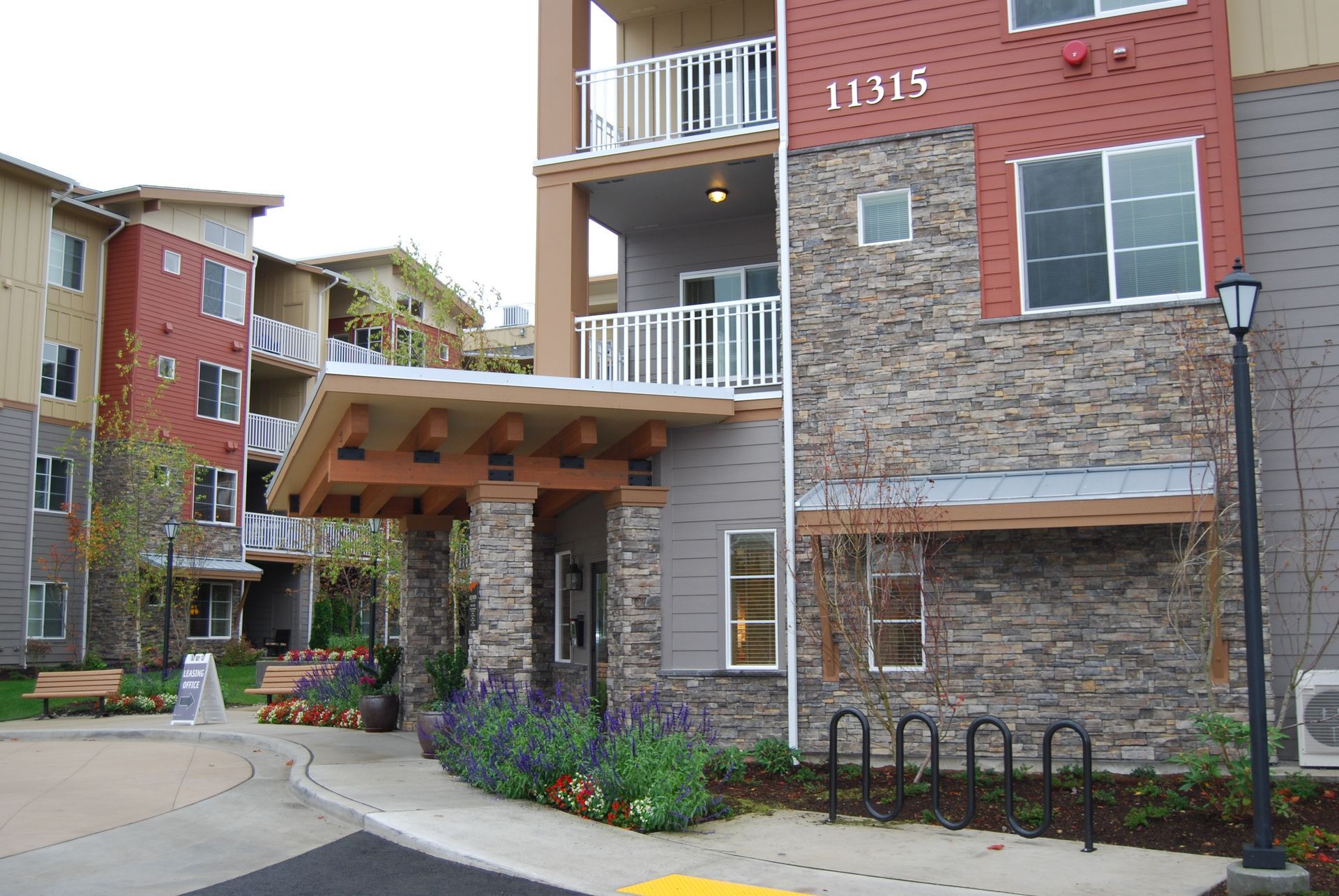 Modern apartment building entrance with balconies, stone and brick exterior, and a covered walkway