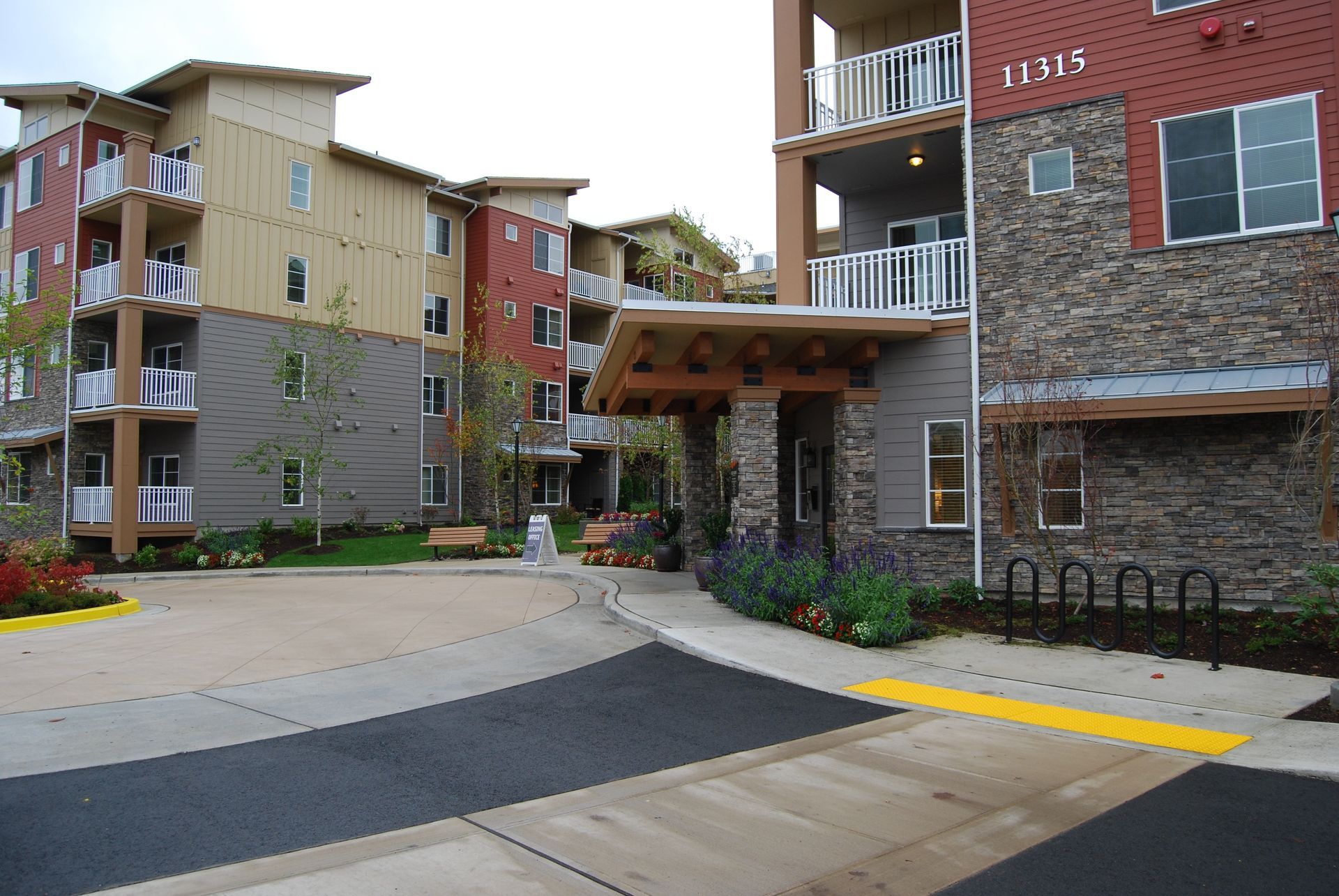 Apartment complex entrance with brick and wood buildings, paved driveway, and bike racks
