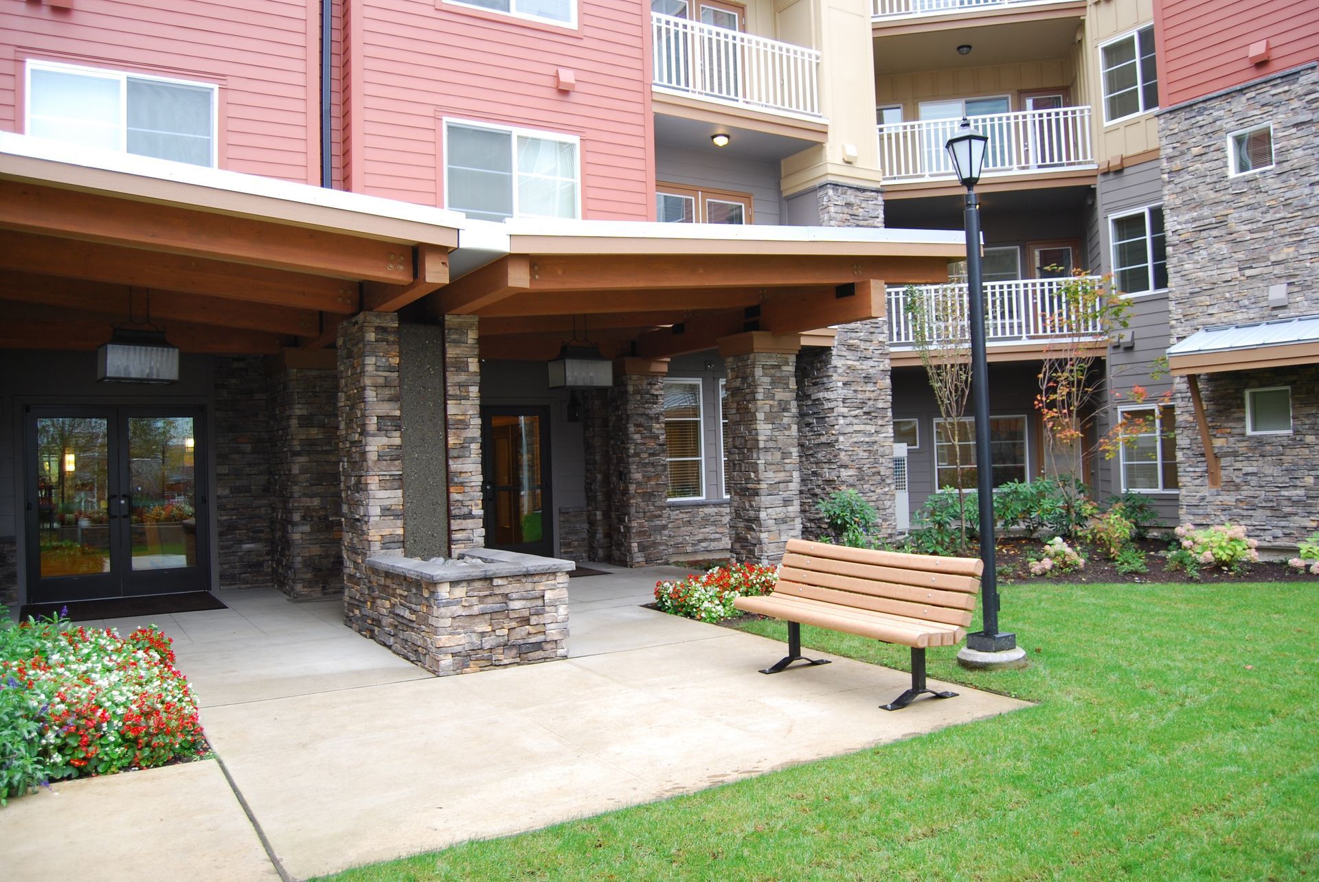 Apartment courtyard entrance with stone columns, a bench, and green lawn