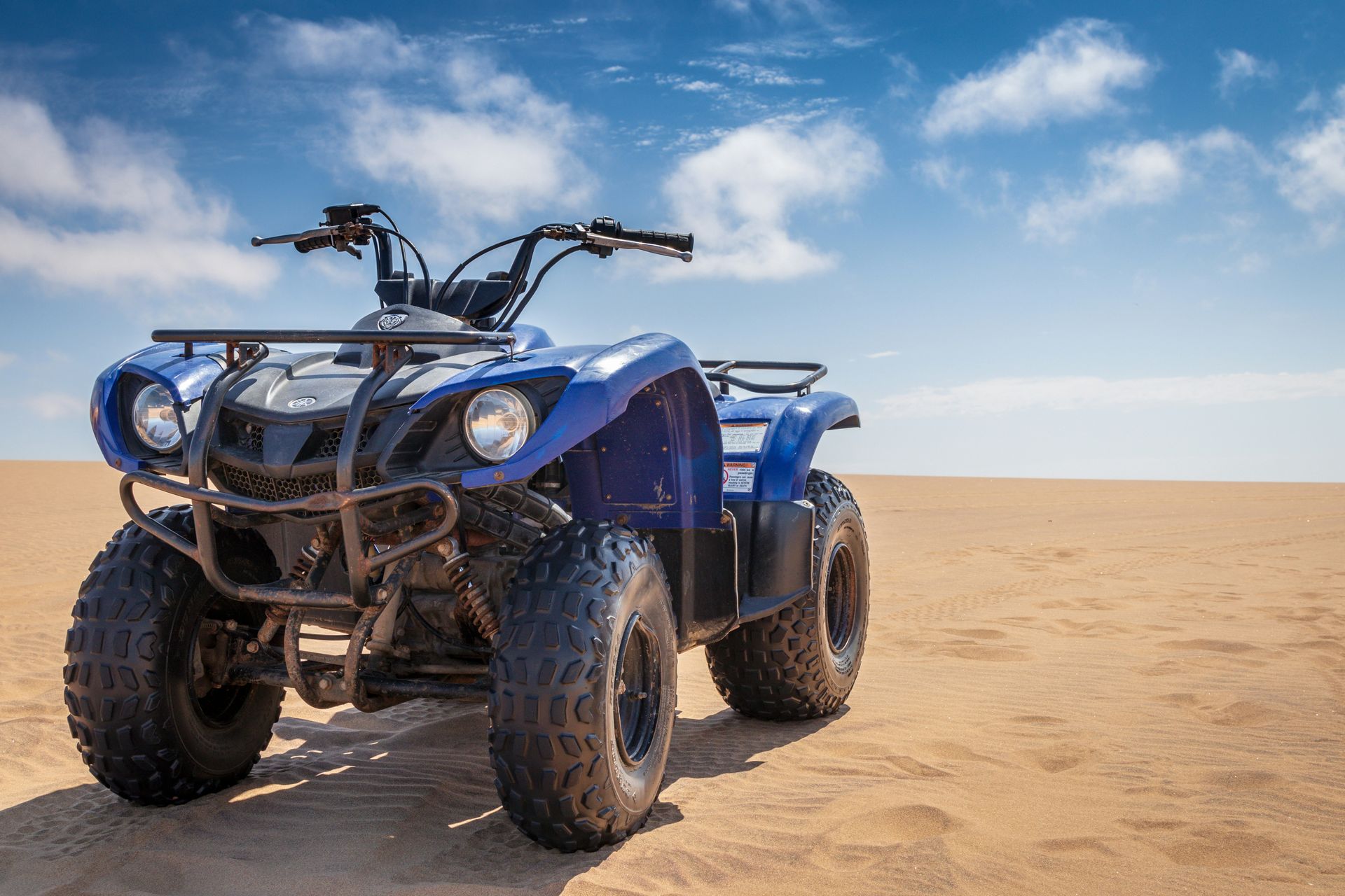 Blue all-terrain quad bike on sand dunes under a bright sky