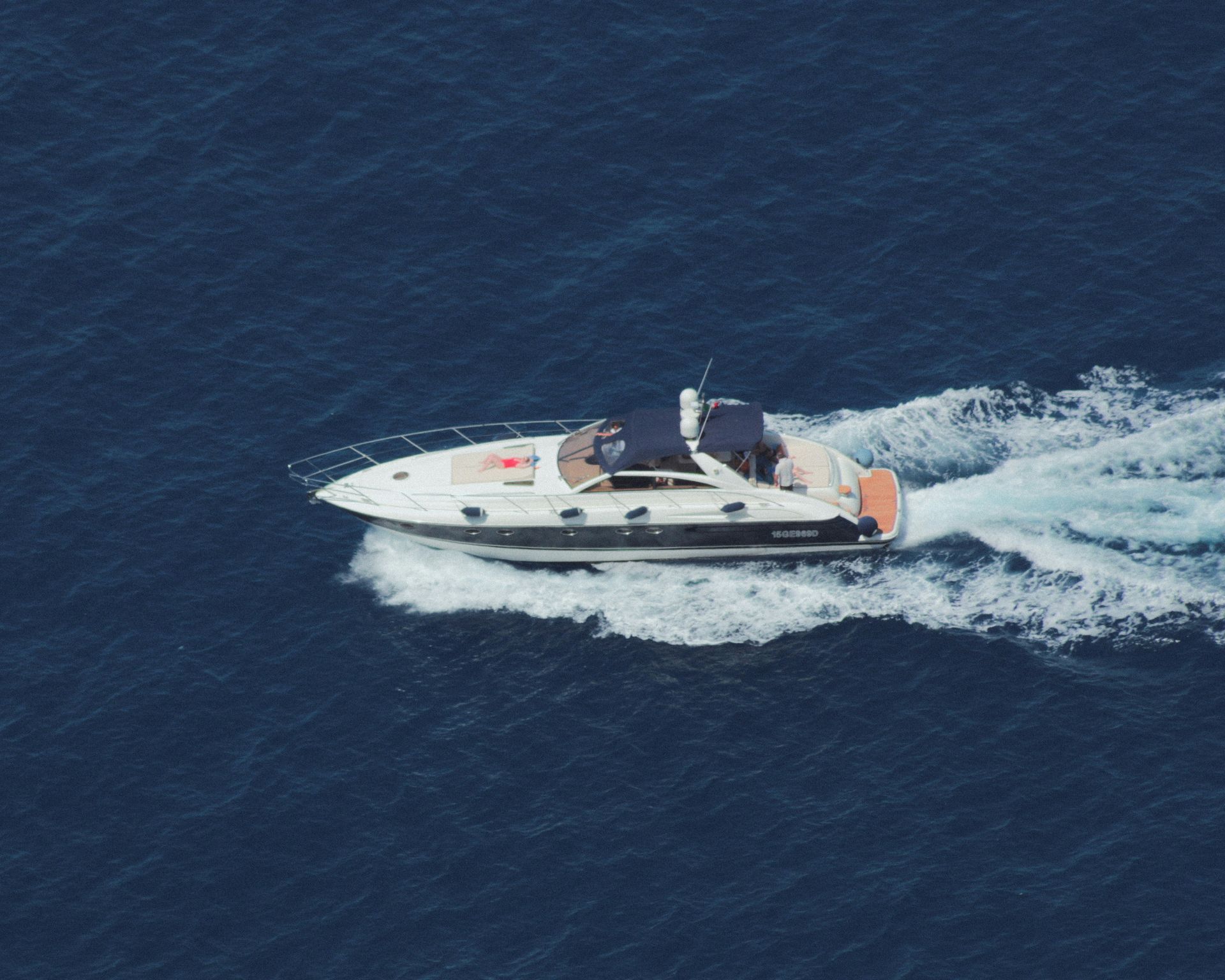 White motor yacht speeding across dark blue ocean, leaving a foamy wake.